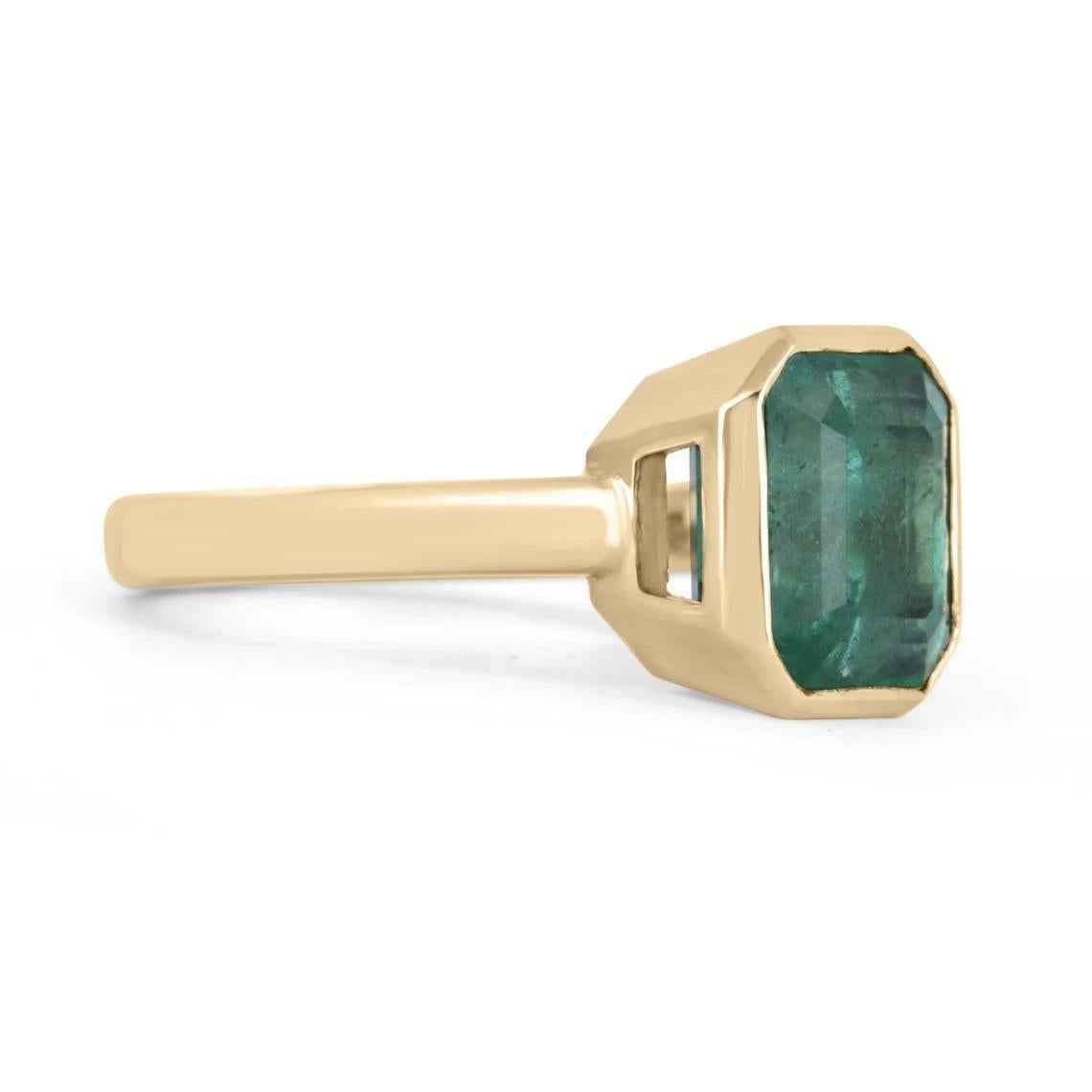 Displayed is a rich vibrant green emerald, solitaire, Asscher-cut bezel ring in solid 14K yellow gold. This gorgeous solitaire ring carries a full 3.17-carat EARTH MINED emerald in a sleek and secure bezel setting. The emerald has incredible