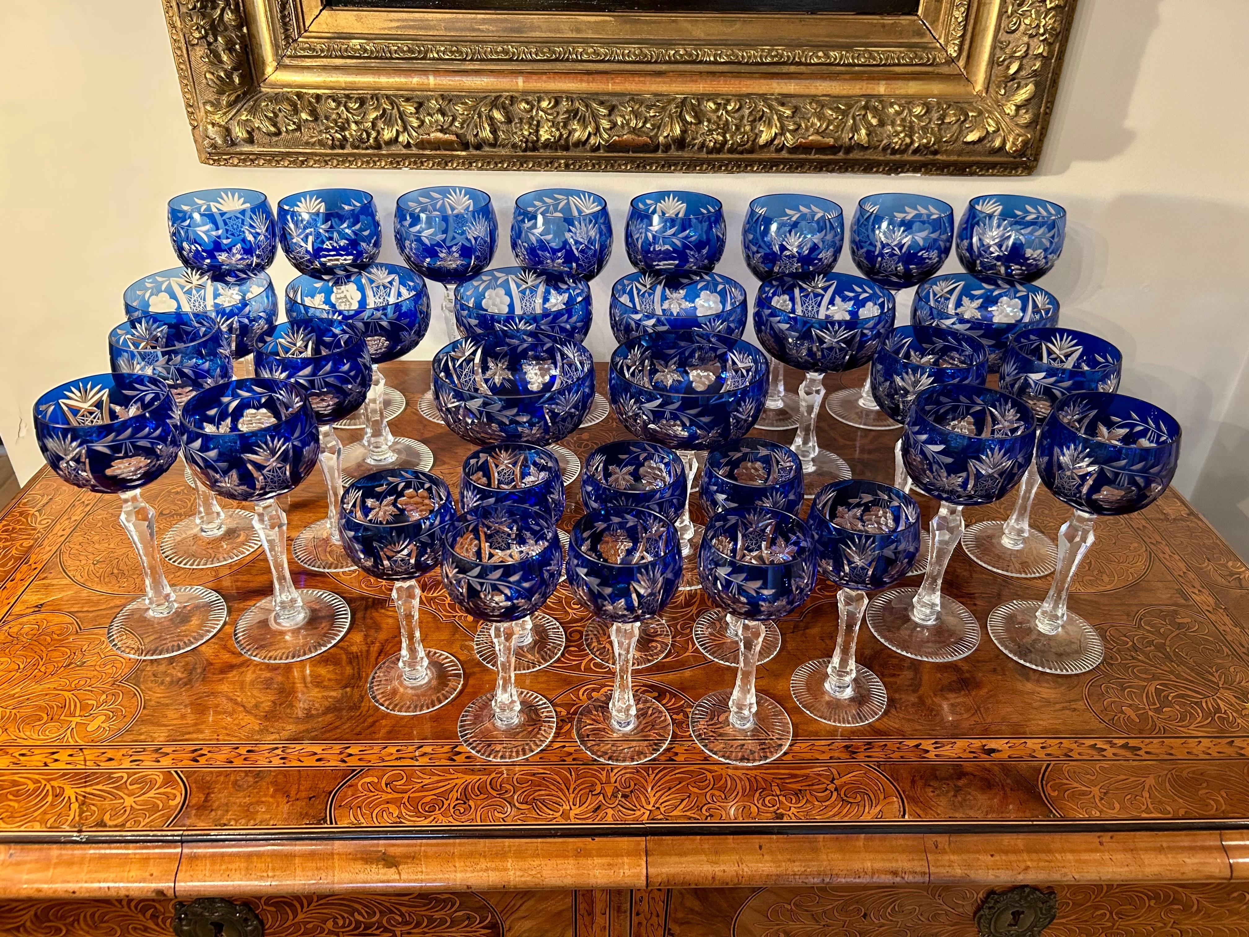 Wonderful set of 32  bohemian cut glasses with  with cobalt bowls and clear faceted stems, heavily engraved with grapevine patterns. This set includes 8 champagne coupes, eight glass wine hocks, eight smaller glass hocks, and eight liqueur