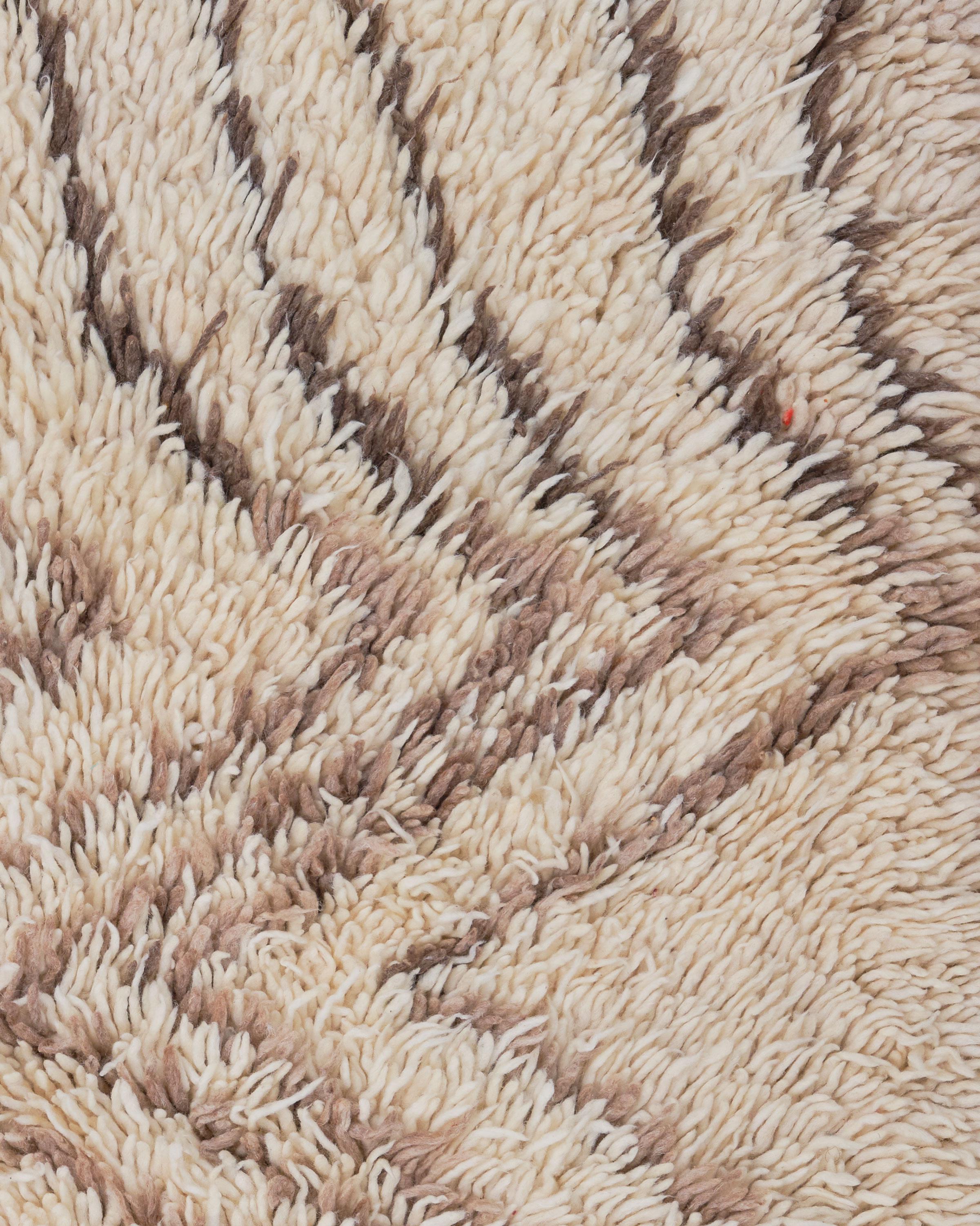 La alfombra Betula es una impresionante pieza marroquí vintage, tejida a mano con lana de oveja 100% natural por hábiles artesanos bereberes. Con un pelo grueso y afelpado, esta alfombra combina cálidos tonos marfil y marrón intenso para crear un