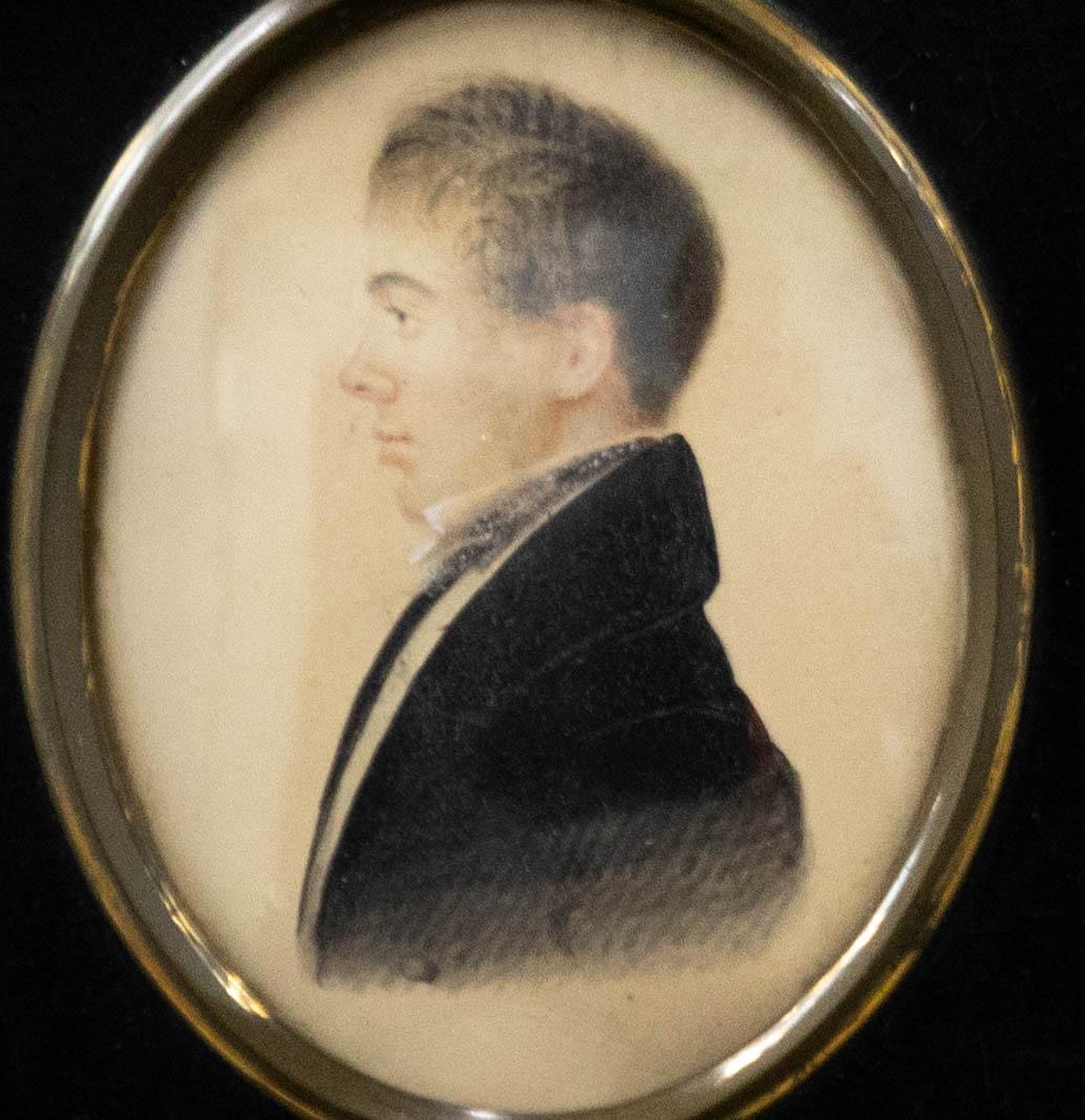 A charming miniature portrait from the early 19th Century, showing a young man in profile. The sitter is wearing a black frock coat with wing collar shirt and cravat. The artist has dated to the reverse. The painting has been presented in a