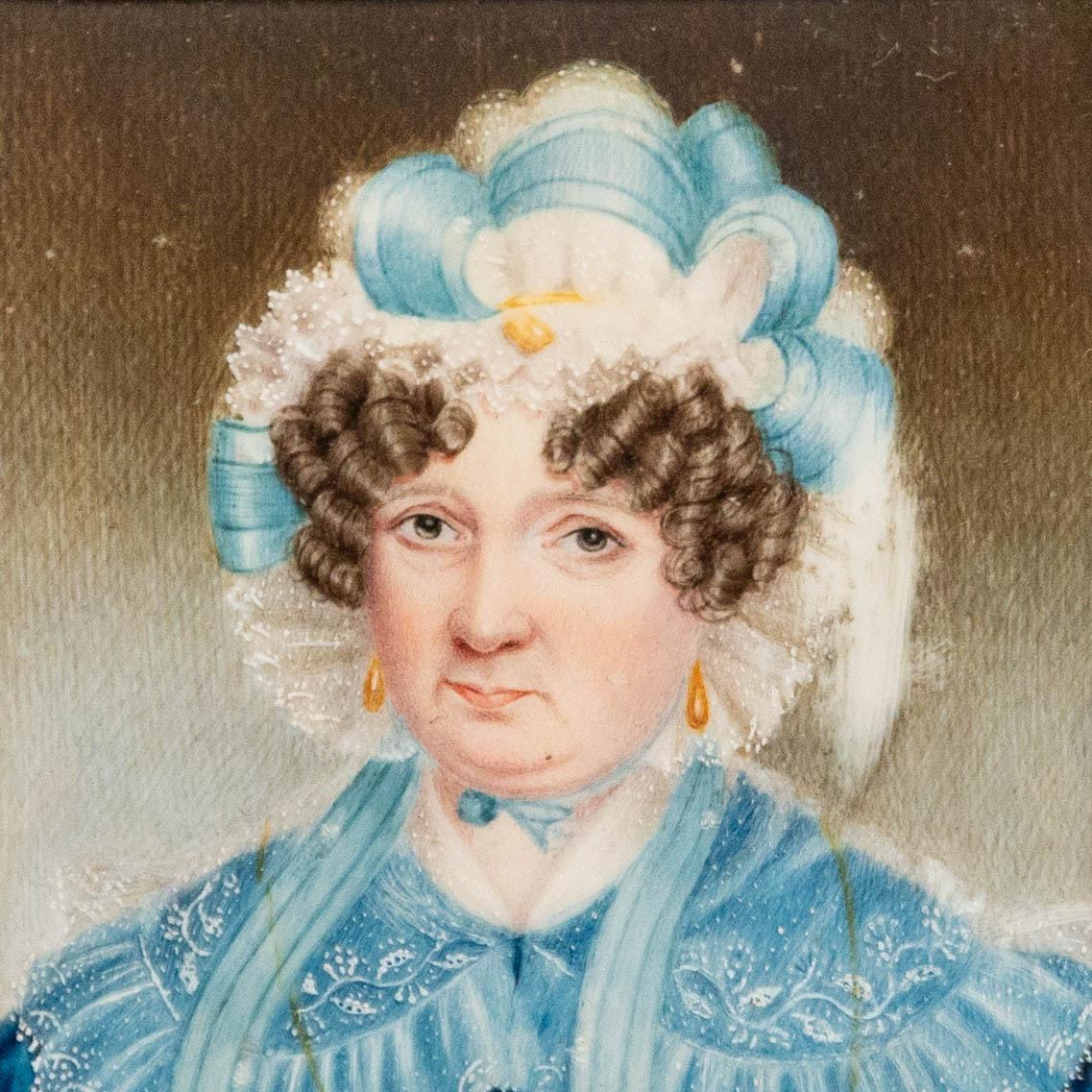 Un exquis portrait miniature géorgien à l'aquarelle, représentant une dame vêtue d'une robe bleue et d'un bonnet élaboré en ruban et en dentelle. Ses bijoux en or et sa dentelle finement détaillée témoignent de sa richesse et de son statut. Non