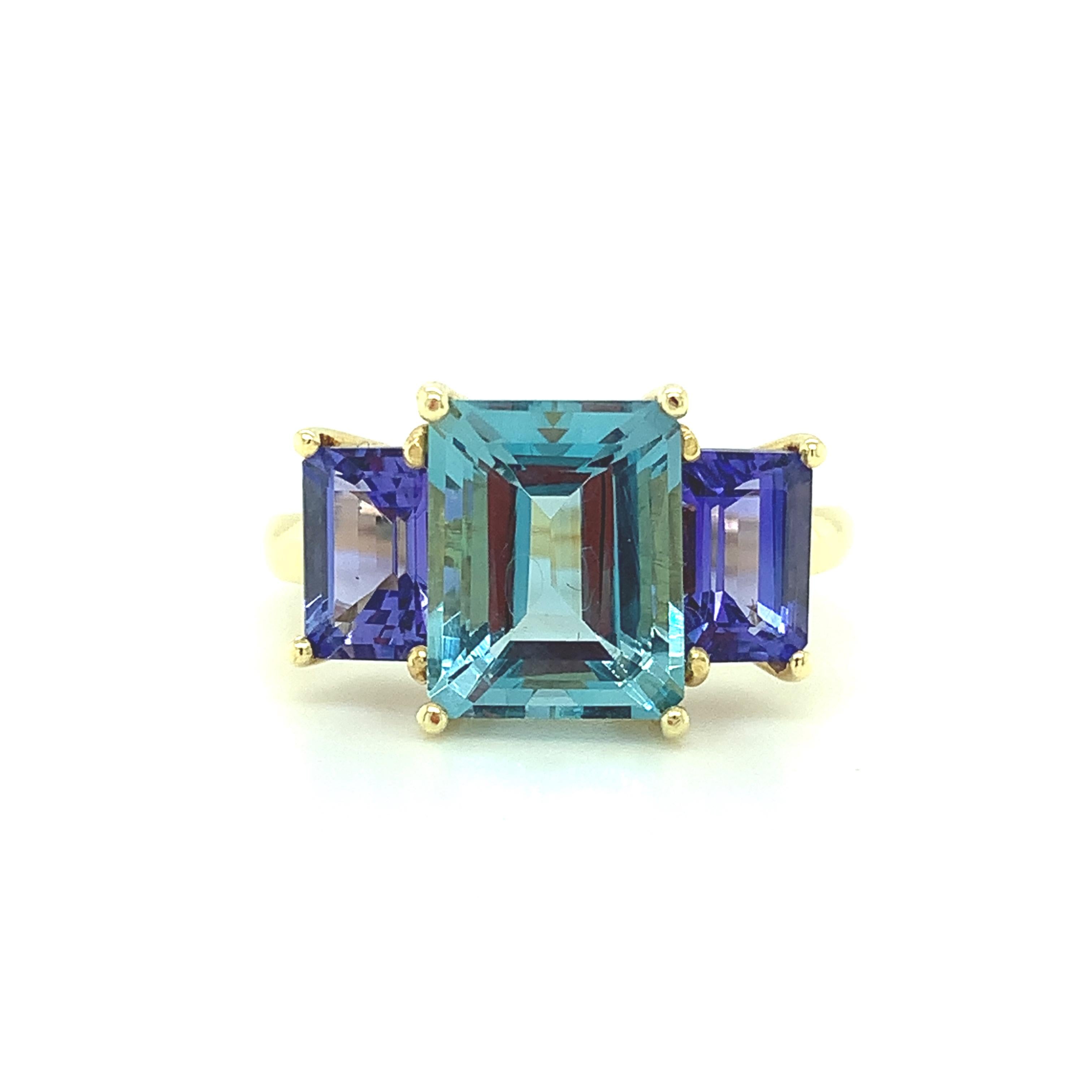 This 18k yellow gold cocktail ring features a fine, emerald-cut aquamarine of unusually fine color and quality! Weighing 3.21 carats, the aquamarine is flanked by two beautifully matched, lavender blue tanzanite baguettes.  This bold and gorgeous