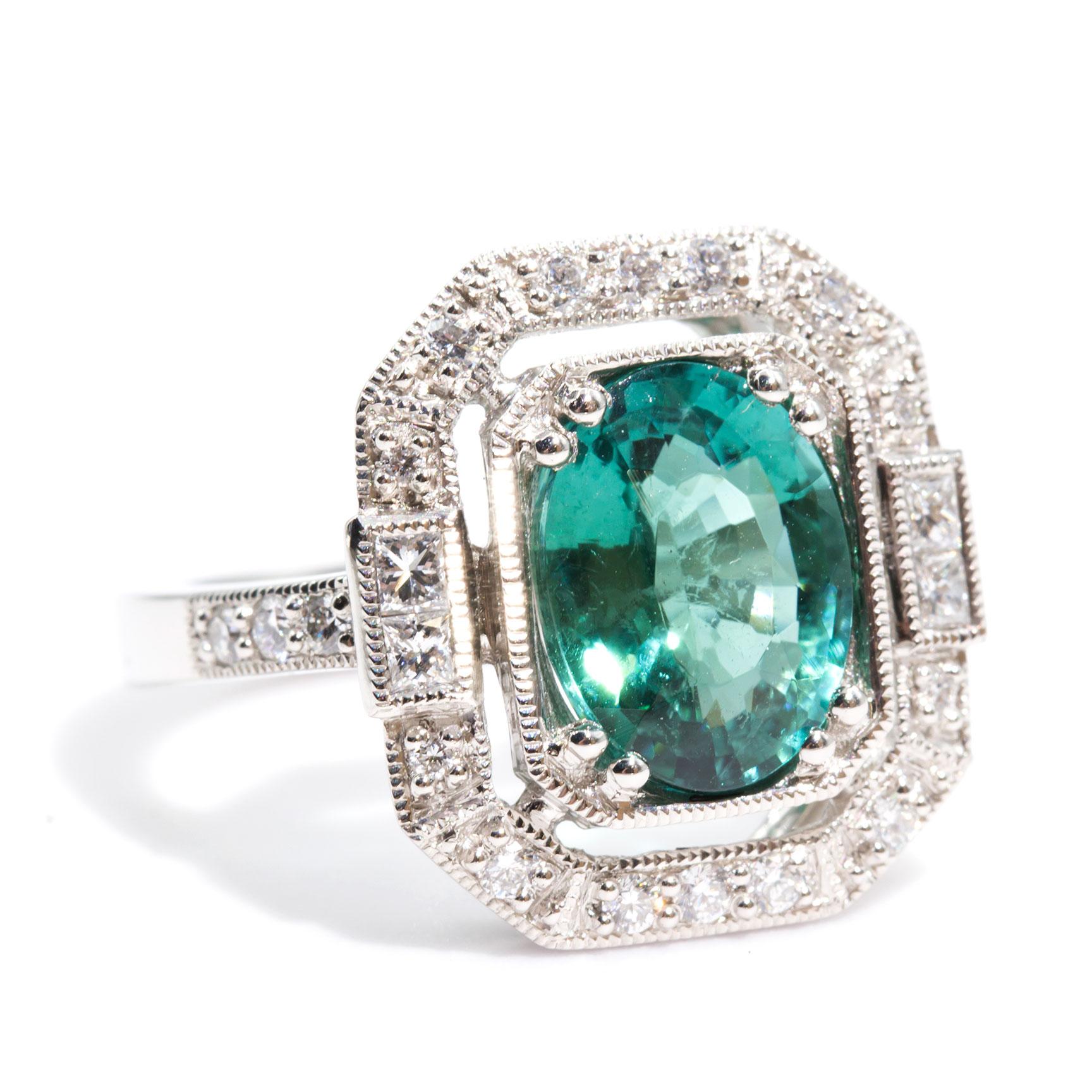 Forged in Platinum, this art deco inspired halo ring features a striking 3.41 oval bright aqua tourmaline complemented by an ornate border of sparkling bead set round brilliant and princess cut diamonds, totalling 0.49 carats. The high polish flat