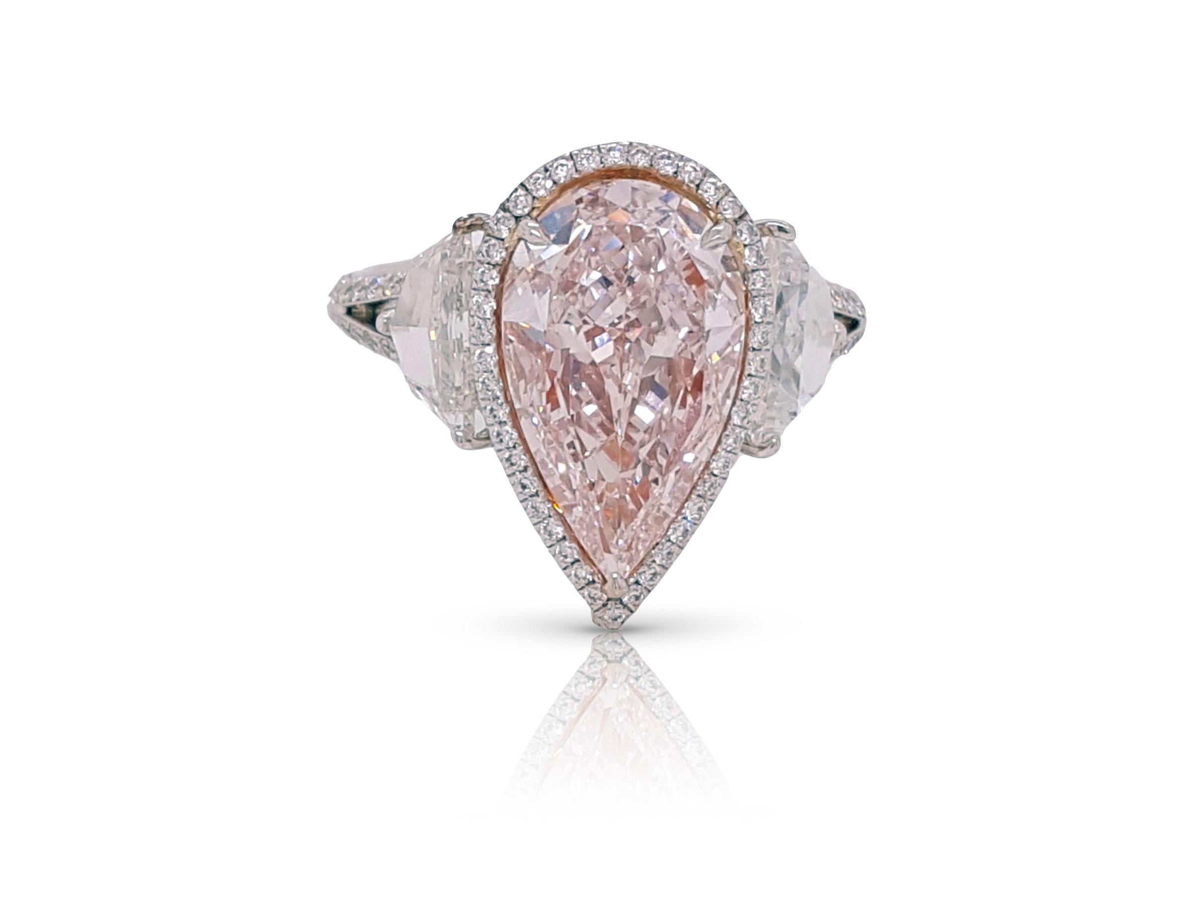 Absolutely stunning engagement ring style showcasing a Fancy Light Pink 3.25 carat pear-shaped diamond certified by GIA as VS2 clarity. The center stone surrounded by a round brilliant white diamonds halo, Flanked by two Cadillac cut diamonds total