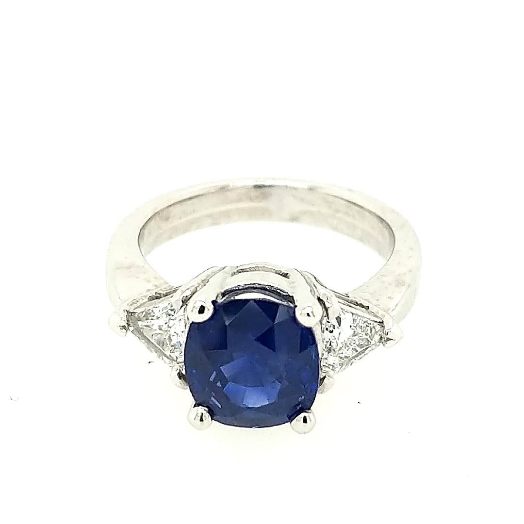 This 3 stone ring is crafted in 18k white gold featuring (1) oval sapphire weighing 3.25ct and flanked by (2) trillions weighing .54cttw with a color of G and a clarity of VS2. The ring is a size 5 3/4. This ring can be sized. 