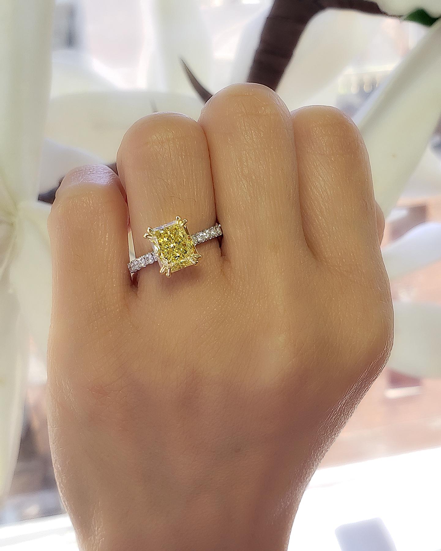 This beautiful elongated canary yellow radiant cut diamond ring features a 2.50 ct. fancy Light yellow radiant cut diamond on the center with a clarity grade of VS2. Complimenting the sides are 0.75 ct. round cut diamond with a color grade of E-F