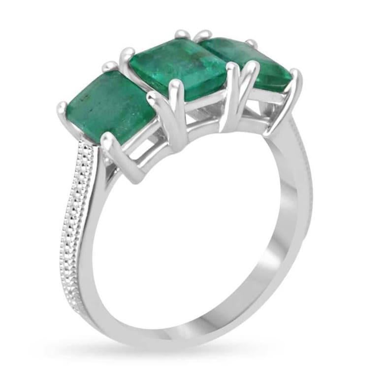 Dieser elegante Ring mit drei Steinen besteht aus einem Trio atemberaubender Smaragde im Smaragdschliff, die vertikal angeordnet sind und durch ihre mittelgrüne Farbe und einen subtilen bläulich-grünen Farbton bestechen. Jeder Smaragd ist sicher in