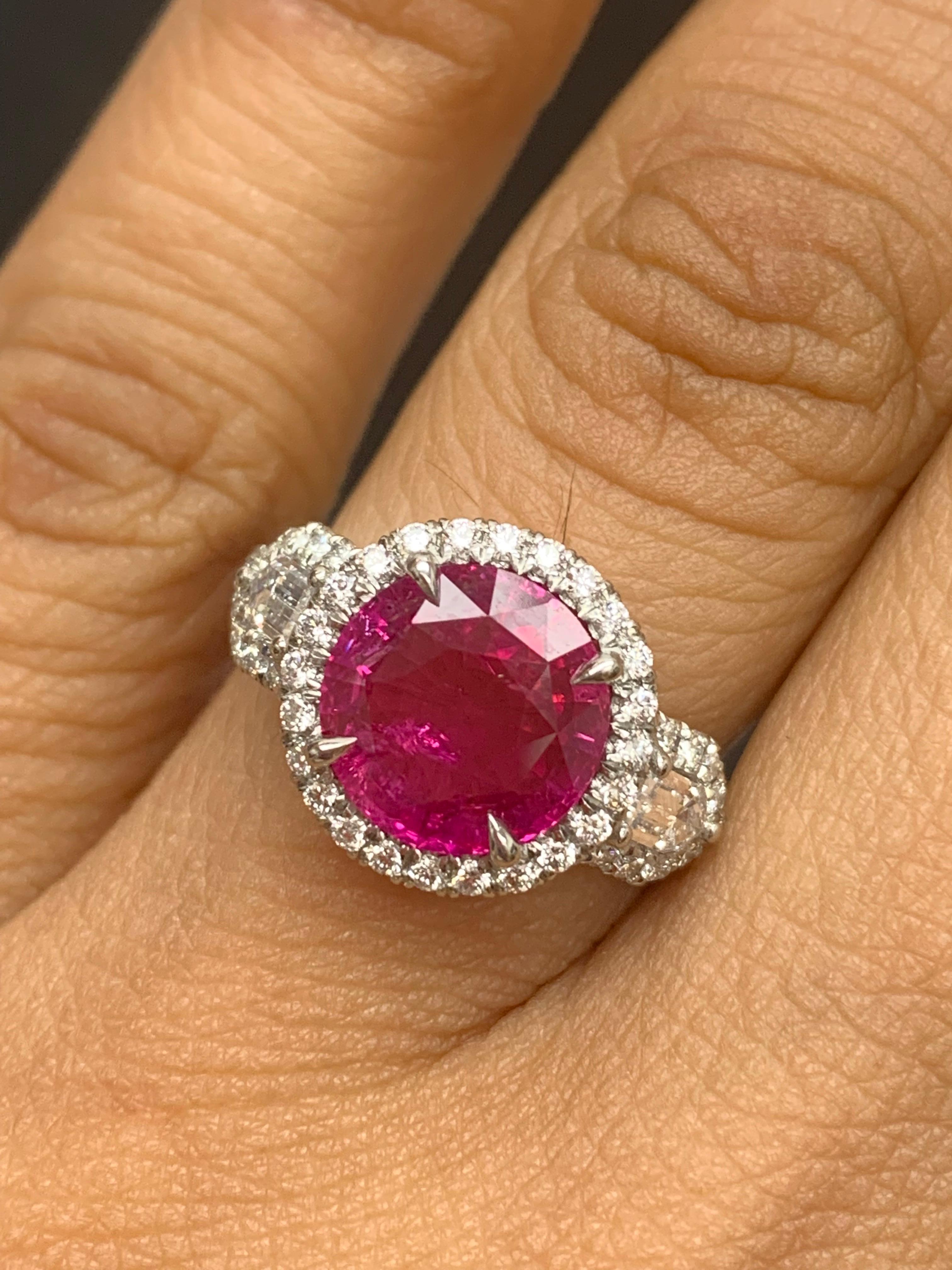 A stunning ring showcasing a rich intense brilliant round cut Ruby weighing 3.28 carats surrounded by a row of diamonds. Flanking the center stone are two bullet-cut diamonds, weighing 0.36 carats total, framed in a brilliant diamond halo. 56 Accent