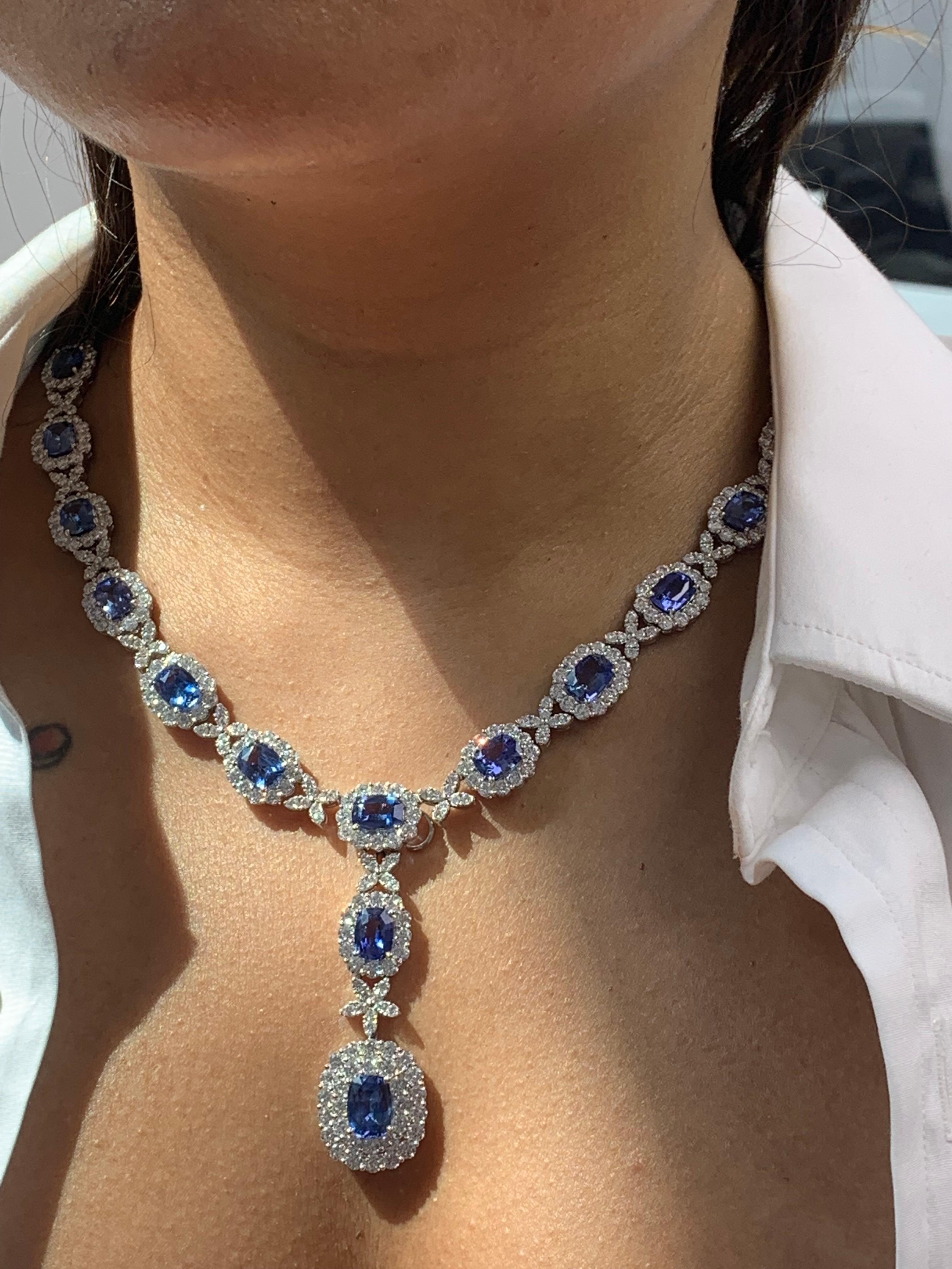 A unique and chic necklace showcasing a drop pendant with 25oval cut blue sapphires, drop pendant 1 sapphire is surrounded by two rows of round brilliant diamonds. The pendant is suspended on a blue sapphire and diamond halo necklace and each