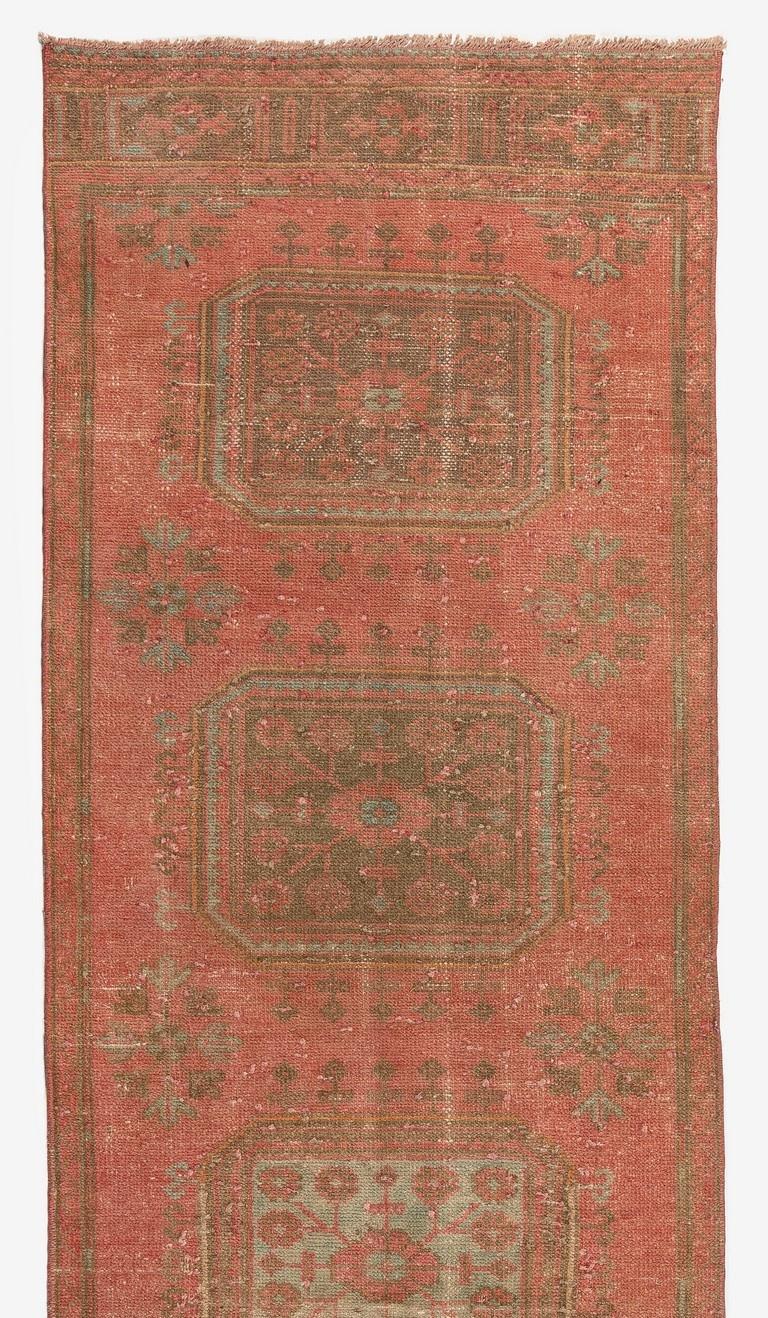 A gorgeous vintage Turkish runner rug with an antiquated look, hand-knotted with low wool pile on cotton foundation. It features geometric medallions decorated with floral motifs in deep sage green and camel colors across the length of a lovely red