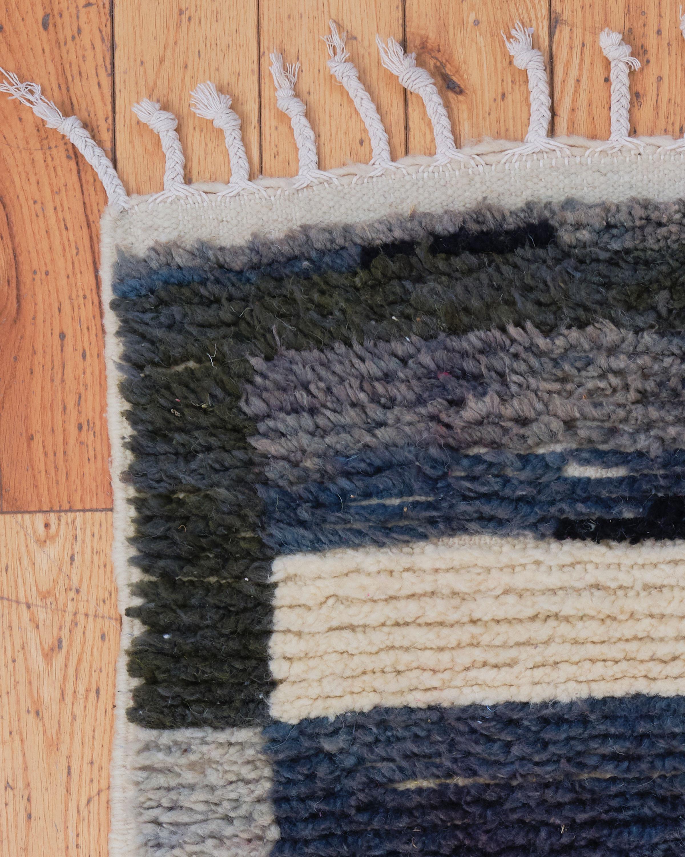 The Castilleja rug is a luxurious vintage Beni Ouarain piece, handwoven by skilled Berber artisans in the Atlas Mountains of Morocco. Featuring a striking combination of gray, black, and blue tones with an inspired pop of pink, this rug blends