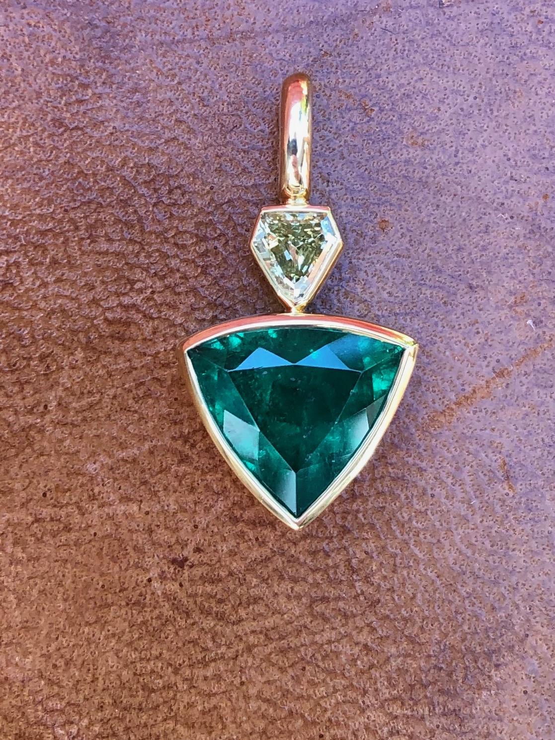 3.3 carat fancy shield cut Colombian Muzo Emerald is set in a hand fabricated 22 karat gold setting with a 0.375 carat vintage fancy yellow diamond. This emerald is vibrant with an alpine green color, and certified 