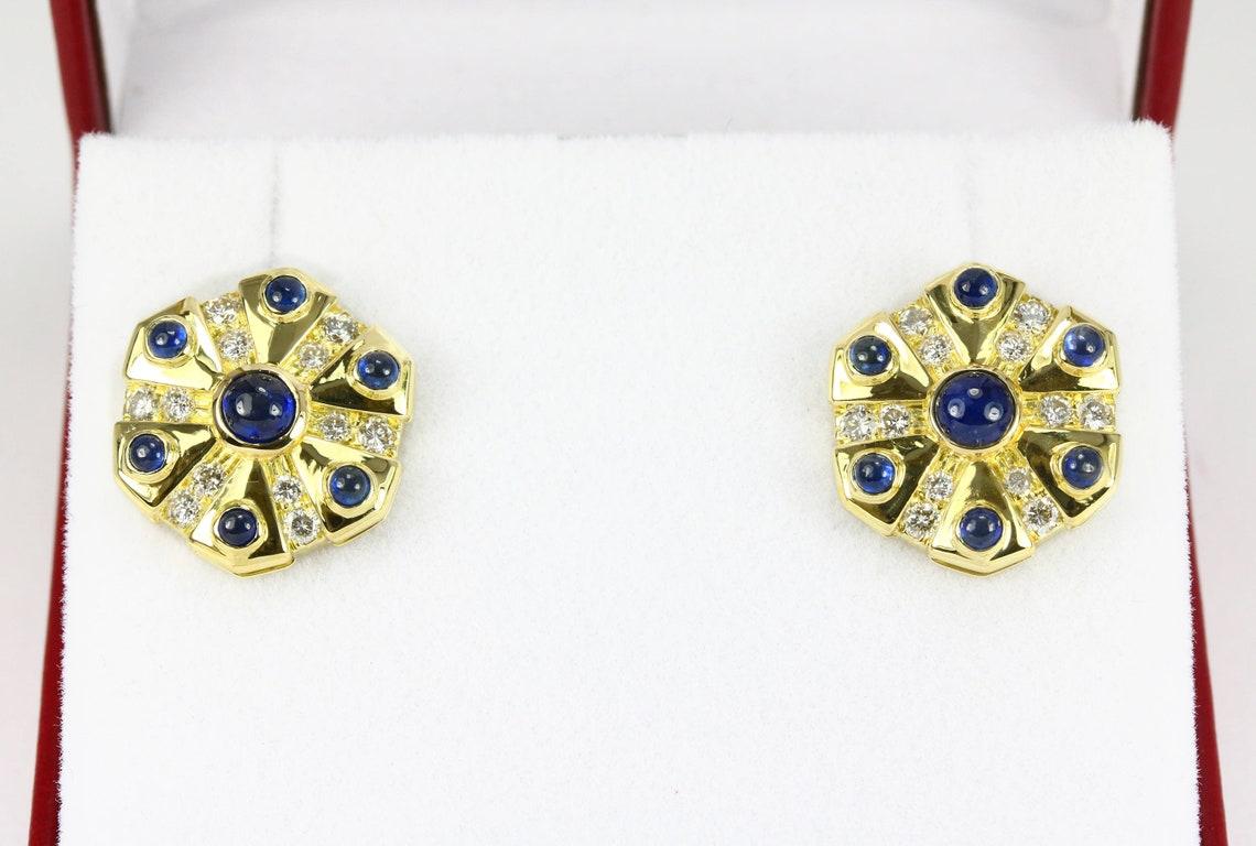 In mostra un sensazionale paio di orecchini a disco con zaffiri e diamanti. Gli zaffiri blu taglio cabochon sono incastonati in un lussuoso oro giallo 18 carati. Queste gemme naturali hanno un'eccellente lucentezza e un'eccezionale chiarezza, e si