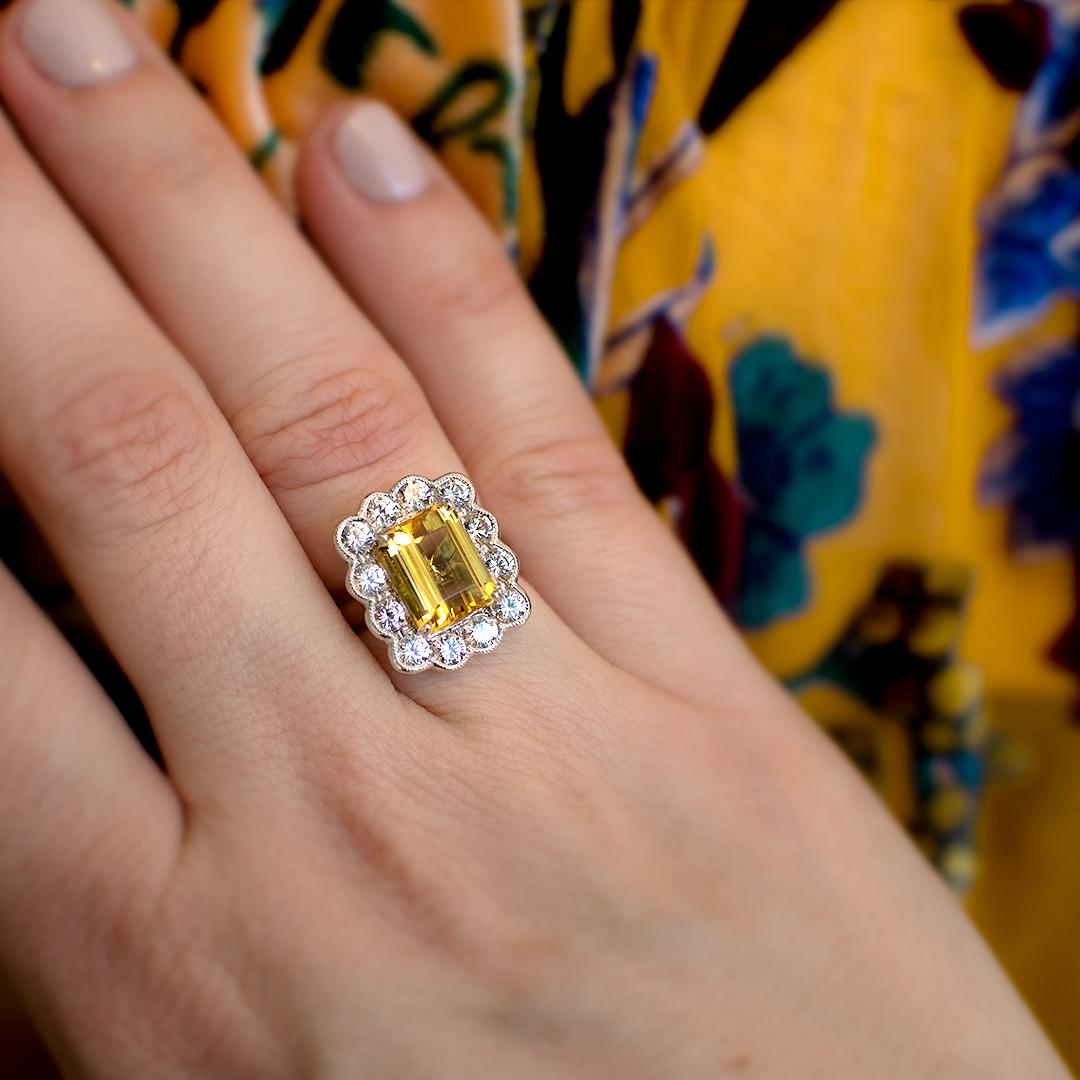A gorgeous Emerald Cut Yellow Beryl (also known as Heliodor) is surrounded by milgrained scalloped white round colourless sapphires for a real Art Deco cluster ring, elegant yet fun look. The Beryl weighs 3.31 carats.

Hand made in 9 Karat white