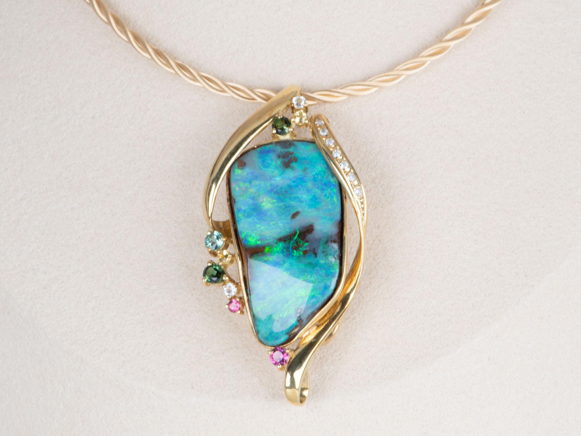  Adorn yourself with this magnificent 33.53ct Australian Boulder Opal pendant brooch combo! This captivating piece features a stunning green blue opal accented by a colorful tourmaline cluster and brilliant diamond border, creating a bold and