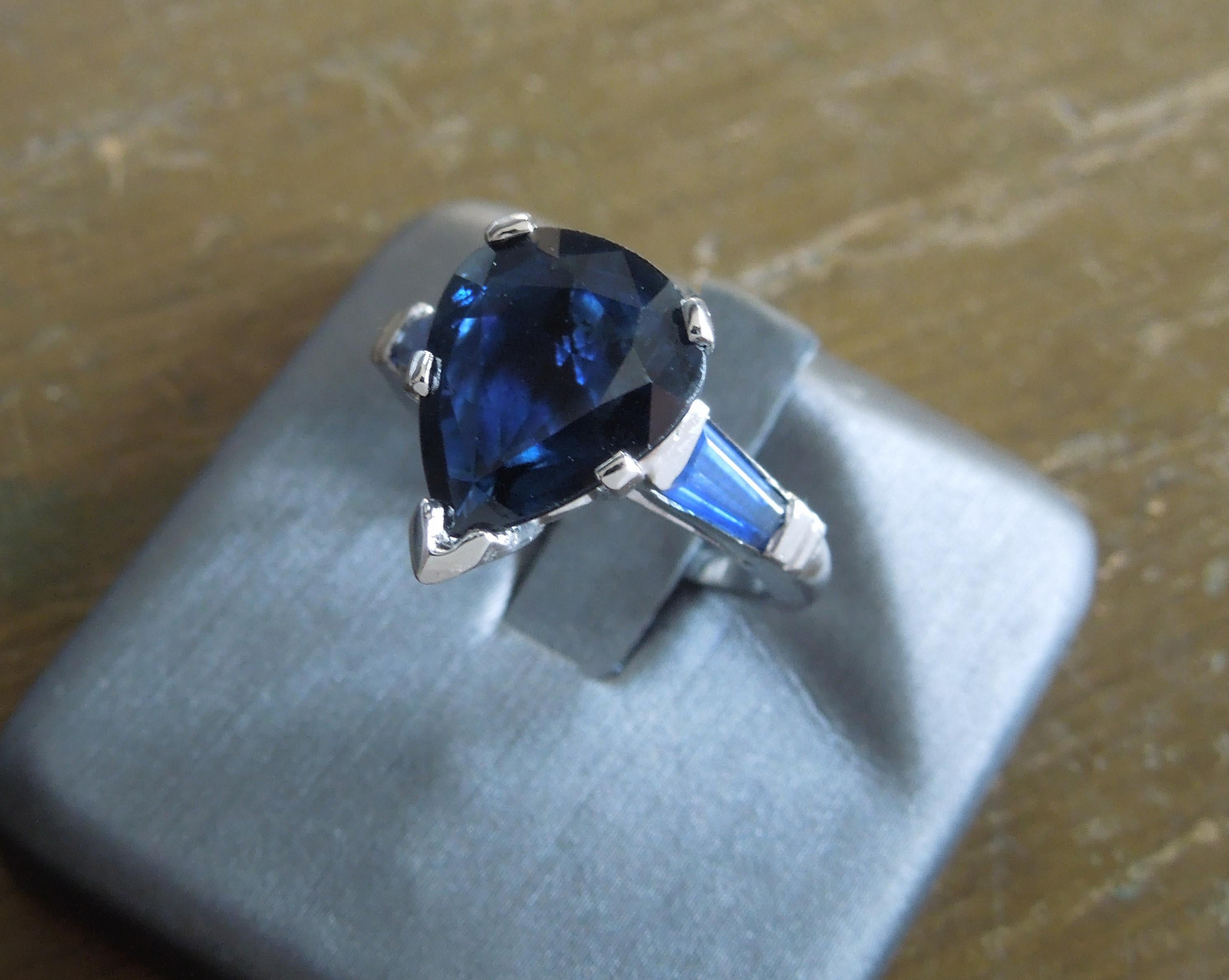 From our Beverly Hills Estate Collection, this Platinum Pear cut Sapphire & Baguette Ring features a central 3.37 carat Pear cut Natural Blue Sapphire at 12mm x 9.5mm at widest, secured in a 5-Prong setting with a secure V-Prong at tip of Sapphire.