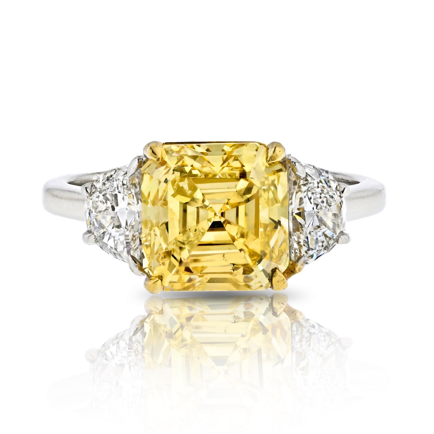 Celebrate your love with the enchanting beauty of this 3.38-carat Fancy Vivid Yellow Asscher Cut Three Stone Diamond Engagement Ring. Meticulously designed, this ring features a captivating center Asscher Cut Diamond and complementary White Half