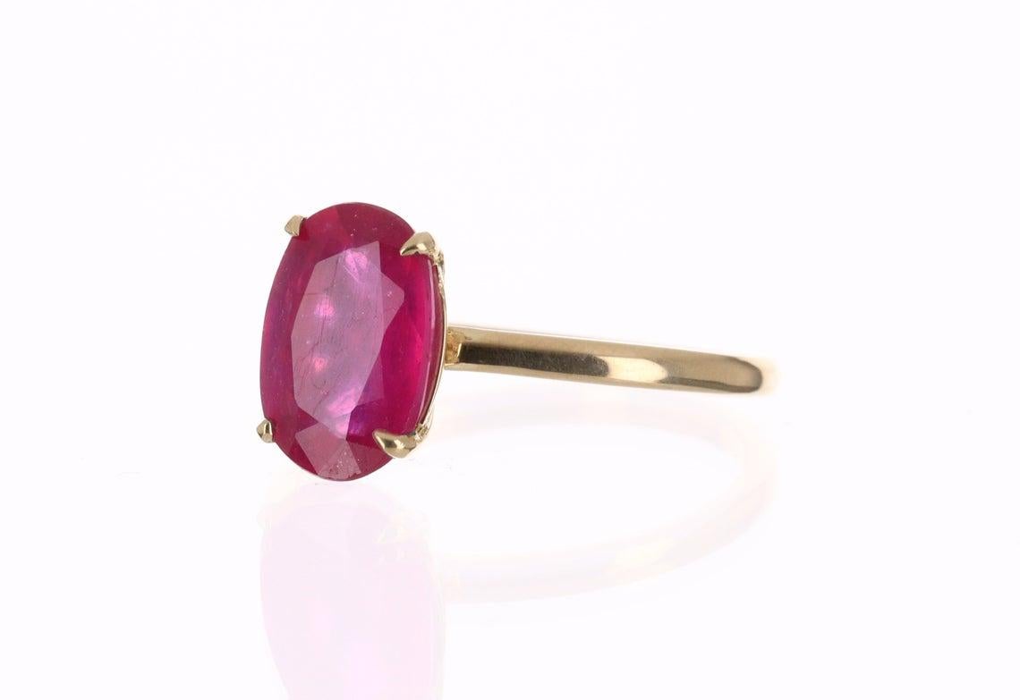 Displayed is a bespoke, ruby solitaire oval-cut engagement/right-hand ring in 14K yellow gold. This gorgeous solitaire ring carries a 3.38-carat ruby in a prong setting. The earth-mined ruby has very good transparency and a jaw-dropping, vivacious,