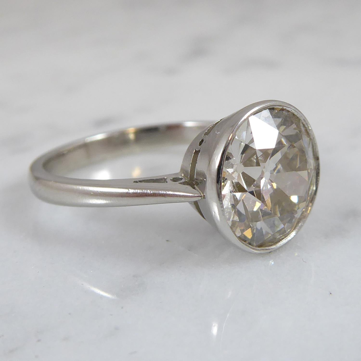 A diamond set single stone ring consisting of an old European cut diamond weighed before resetting as 3.39ct and measuring 9.60mm-9.40mm x 5.52mm deep.  Rub over set to a circular white collet, to tapering chenier inserted shoulders and a plain