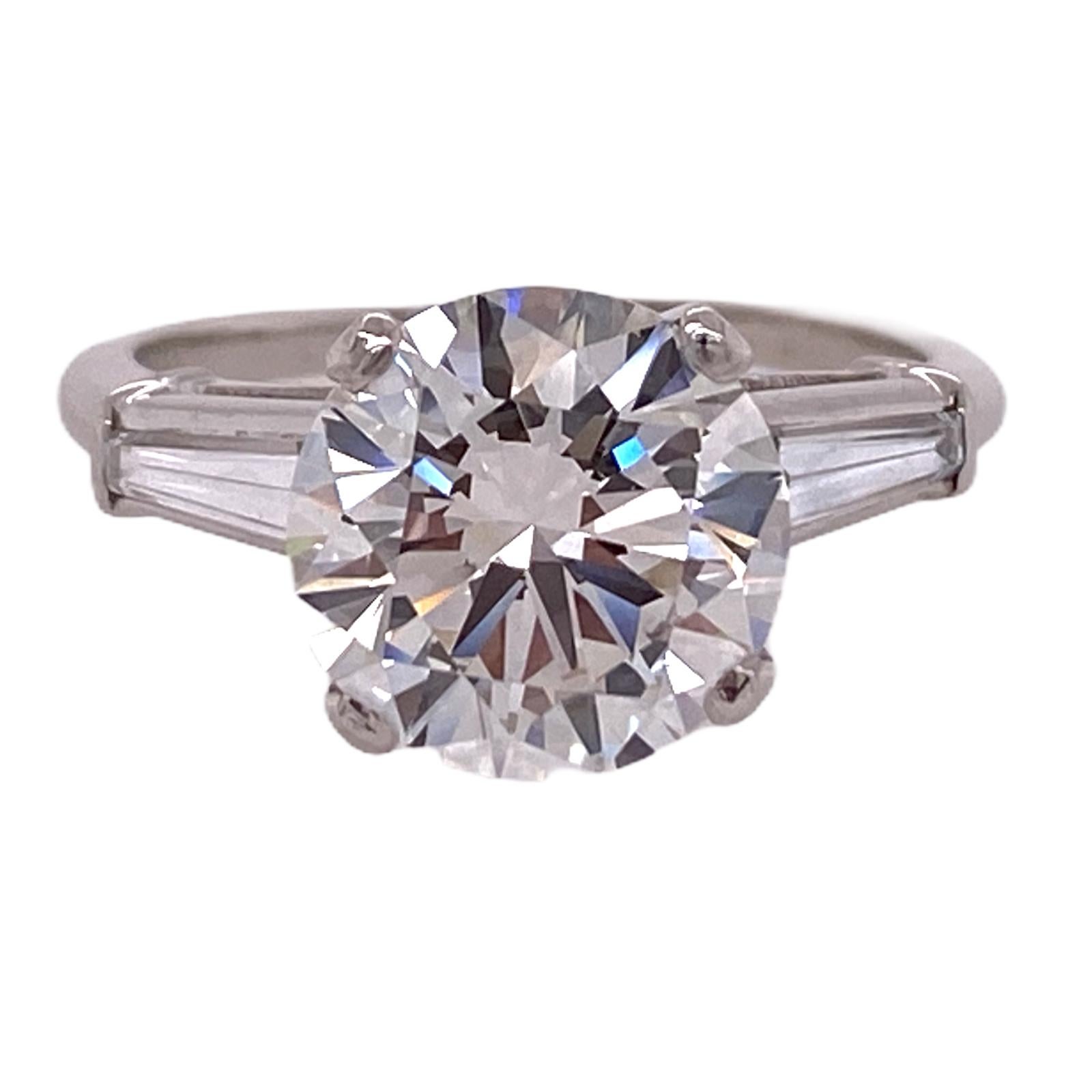 Stunning diamond engagement ring hand crafted in platinum. The round brilliant cut diamomd weighs 3.39 carats and is graded by the GIA J color and VS1 clarity. The sparkling center diamond is flanked by two tapered baguettes weighing .30 ctw. The