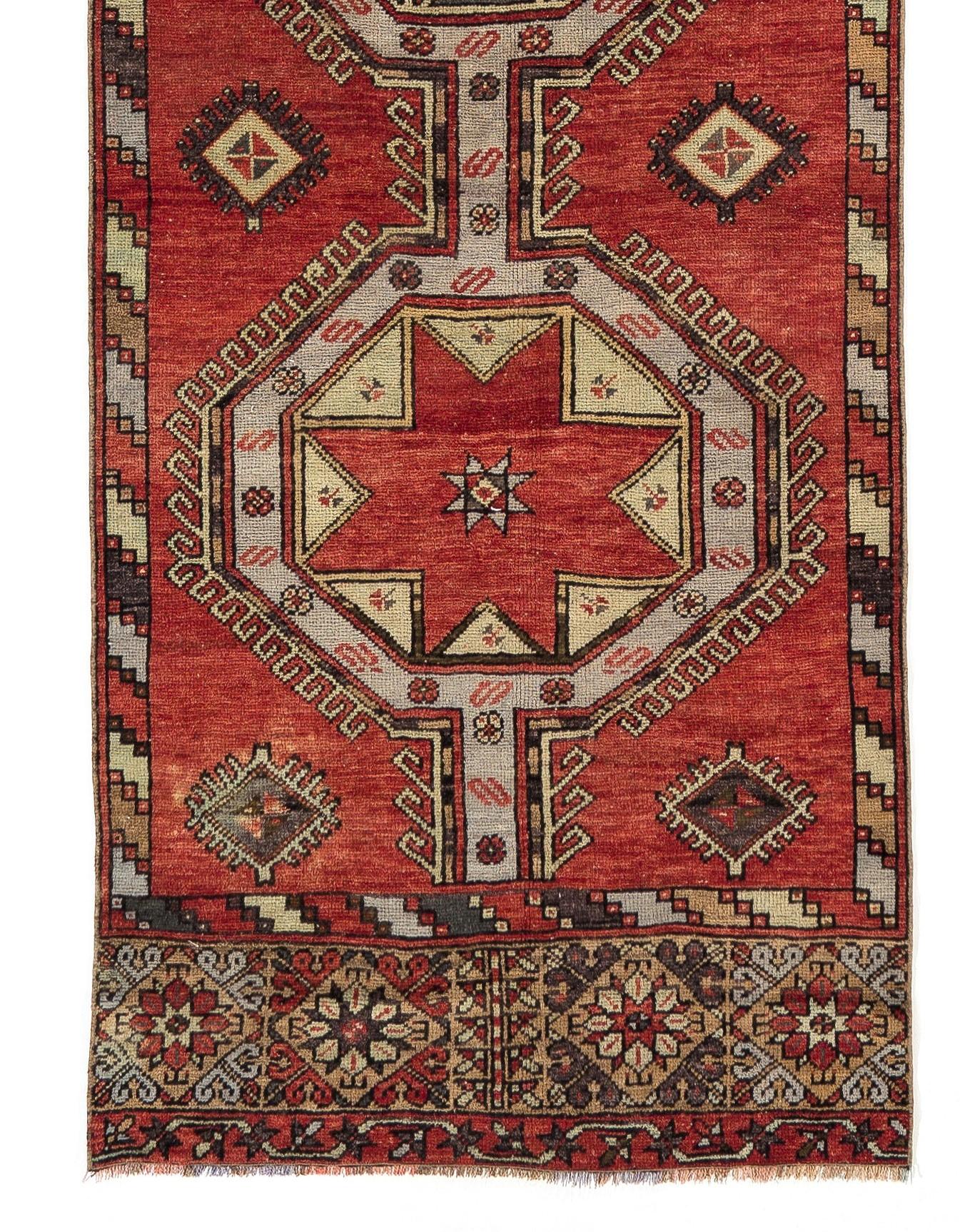 A 1950s hand-knotted runner rug from Central Turkey featuring an eye-catching geometric/star medallions design against a deep tomato red field and and elaborately decorated borders at the top and bottom ends. The rug has soft medium wool pile on