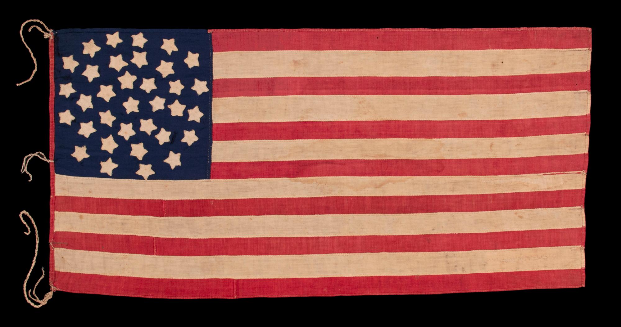 34 STAR ANTIQUE AMERICAN FLAG OF THE CIVIL WAR PERIOD (1861-63), IN A TINY SCALE AMONG PIECED-AND-SEWN FLAGS OF THE PERIOD, WITH A TRIPLE-WREATH CONFIGURATION, AN ELONGATED FORMAT, AND ENTIRELY HAND-SEWN;  FOUND WITH A LETTER FROM JOHN W. RUDE OF