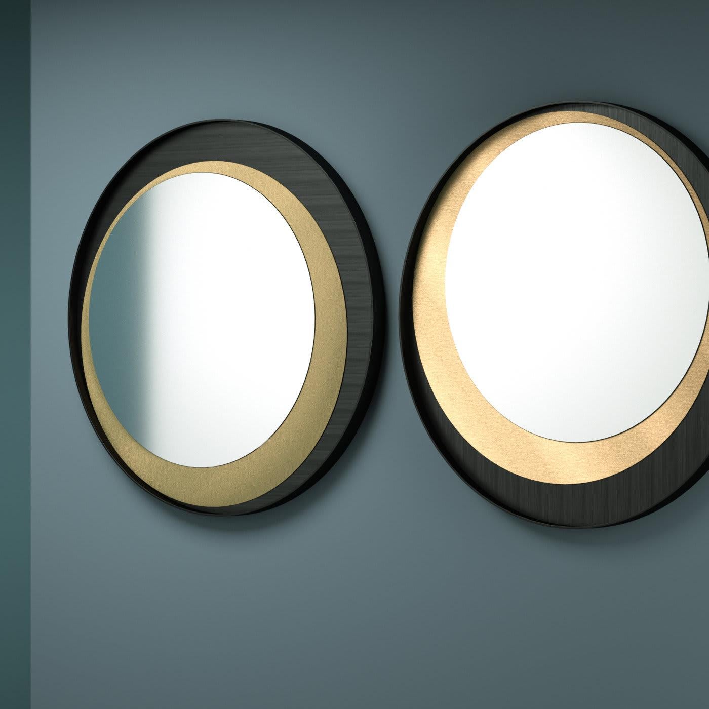 In this elegant wall mirror, a single round metal sheet finished in black frames a second round metal insert that contains the mirror. This striking overlap results in an iconic design that can be displayed in four different ways, thanks to the four