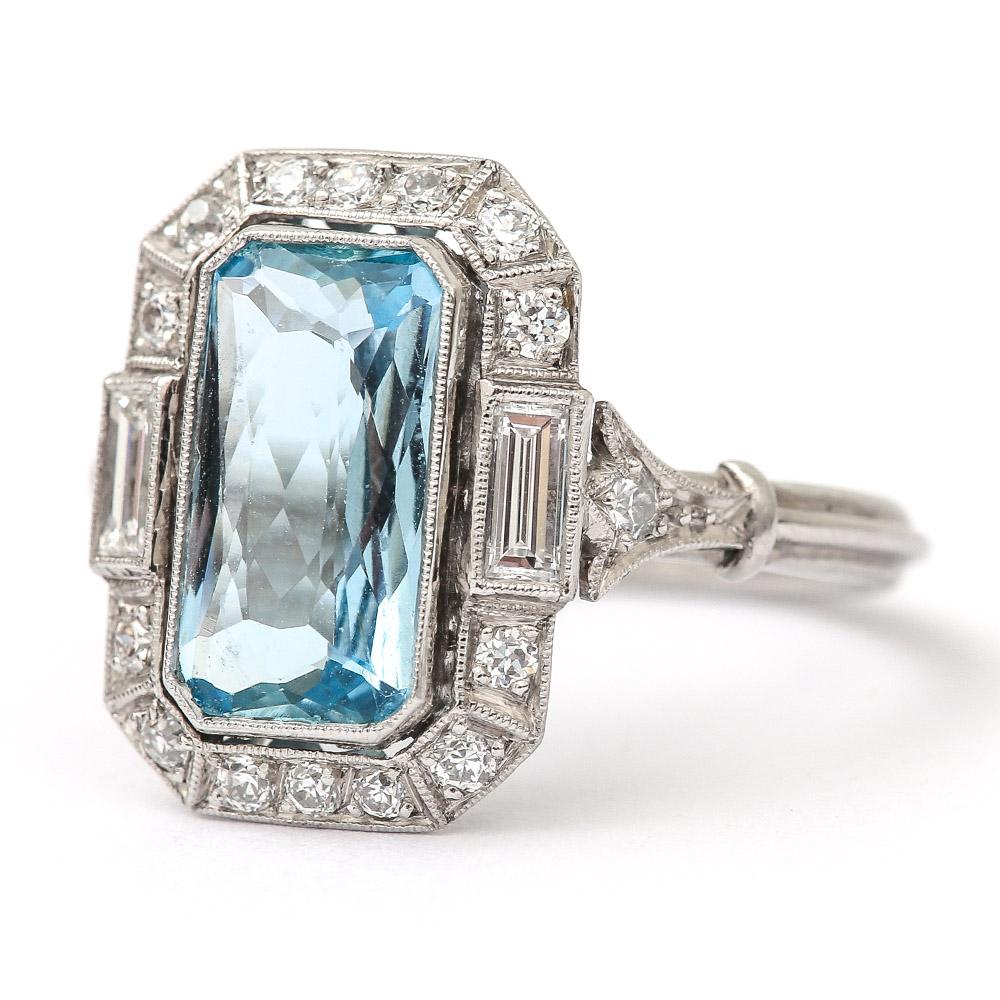 A super original Art Deco aquamarine and diamond ring set with a cushion cut, intricately faceted est. 3.40ct aquamarine flanked by two baguette diamonds (est. 0.20cts each). A further 14 brilliant cut diamonds estimated at 0.02cts each, all