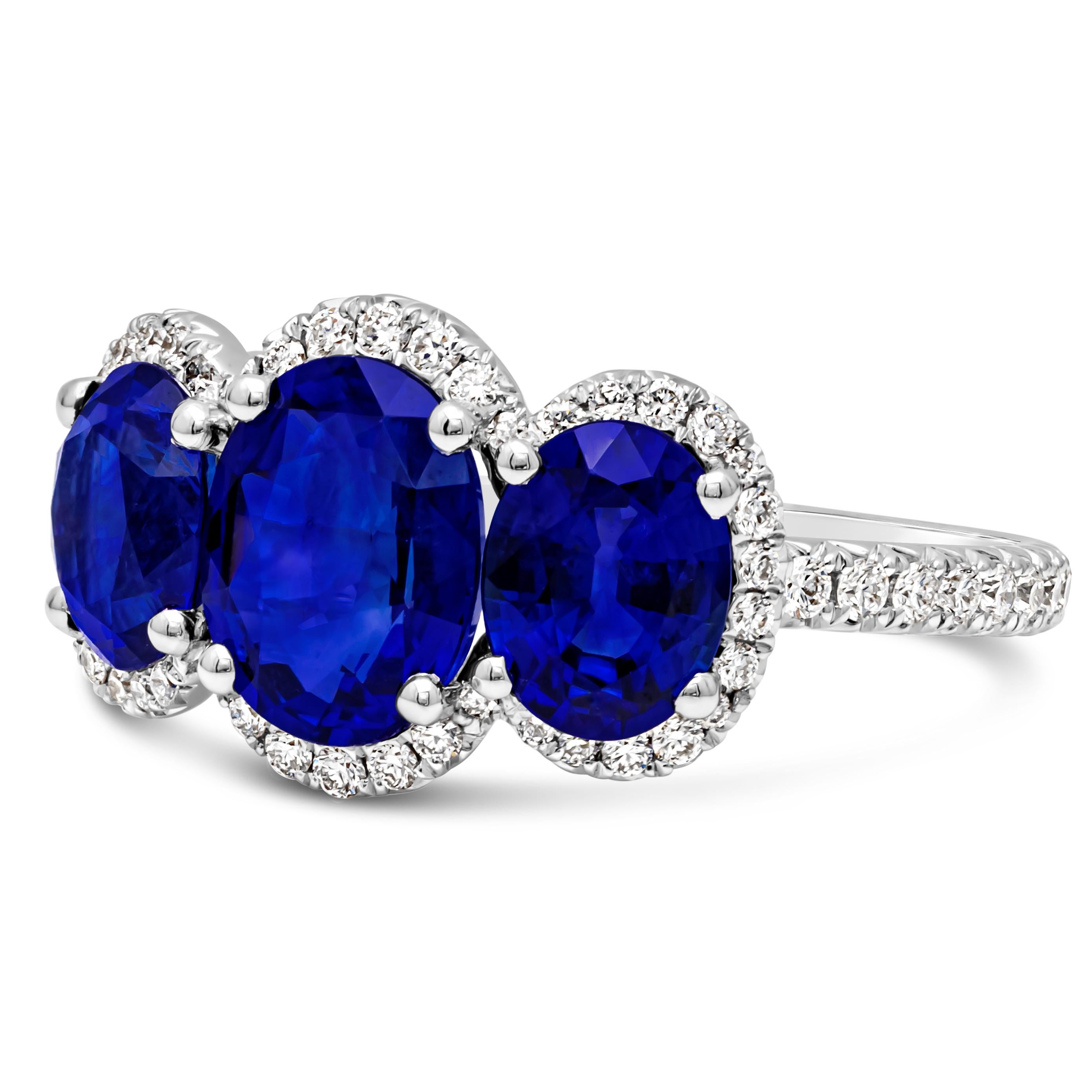 This classy and elegant three-stone halo engagement ring showcasing three oval cut natural blue sapphire weighing 3.40 carats total, surrounded by a row of round brilliant diamonds in a halo design weighing 0.4 carats total. Accented with brilliant