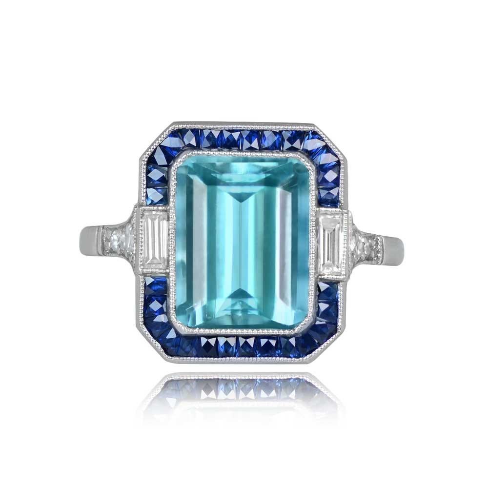 An elongated gemstone and diamond ring showcasing a natural emerald-cut aquamarine weighing 3.40 carats. Surrounding the center gemstone is a halo of calibre French-cut natural sapphires and elongated baguette-cut diamonds, enhancing its brilliance.