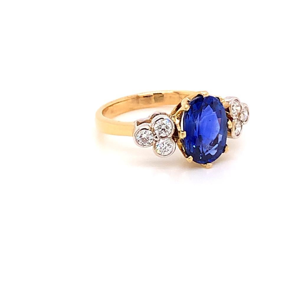 This regal ring features a 3.42 Carat oval Blue Sapphire at its centre, held in a claw setting on an 18K Yellow Gold band. On either side of it, in a rub-over setting, are 3 scintillating round brilliant Diamonds, weighing a total of 0.37 Carats.