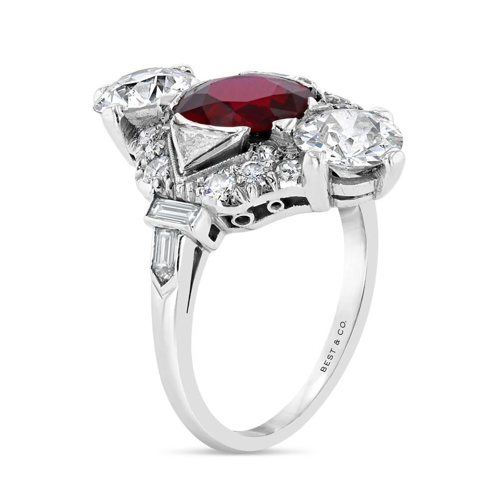 A beautiful 1.56 carat oval ruby is centrally set and flanked top and bottom with two round brilliant cut diamonds each weighing half a carat.  Round, triangular, baguette, and arrow-shaped diamonds complete the intricate mounting.  Set in