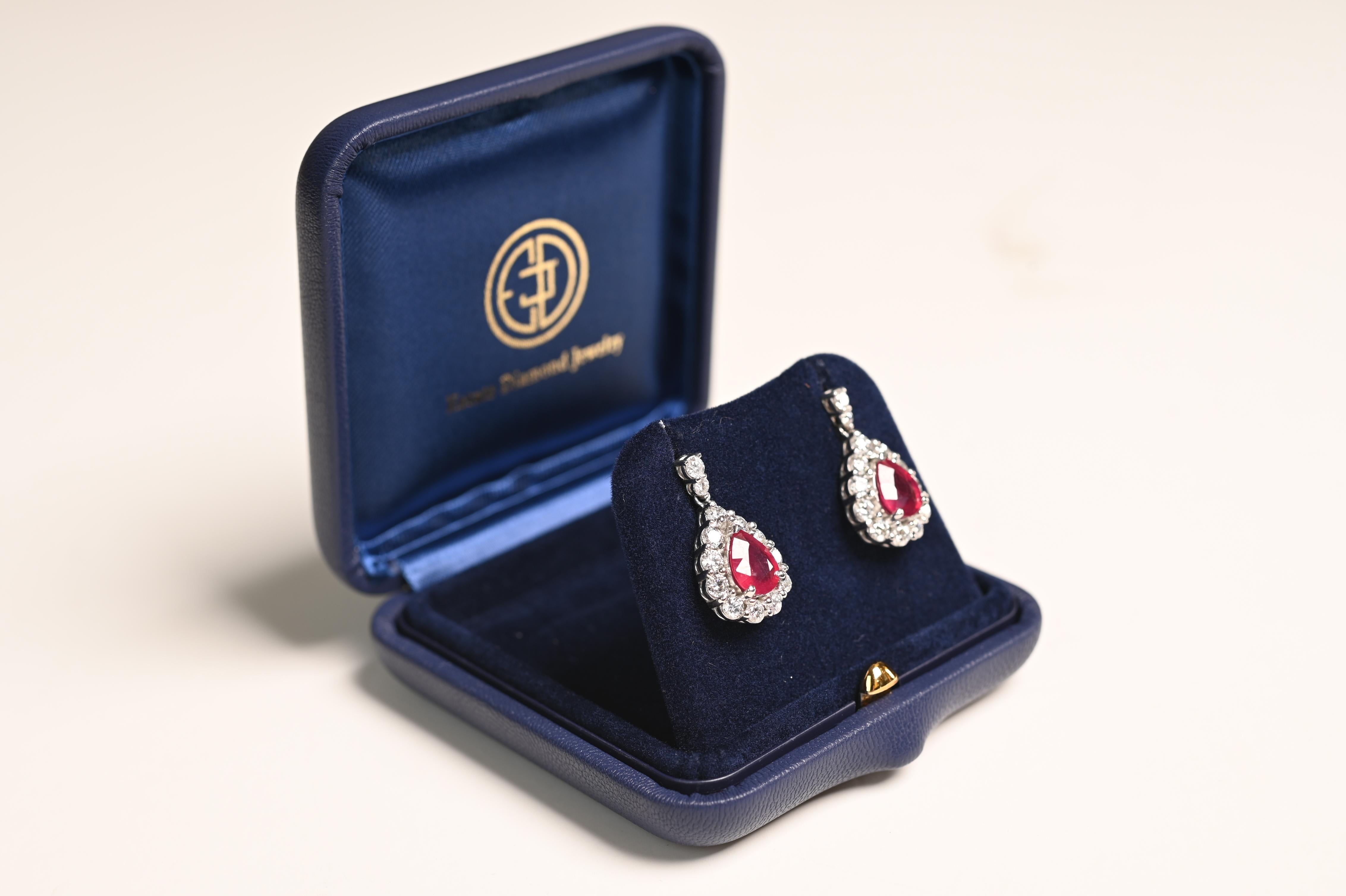 This exquisite pair of ruby and diamond earrings is a testament to timeless elegance and craftsmanship. At the heart of each earring lies a captivating pear-shaped Burma ruby, boasting a combined weight of approximately 3.42 carats. These rubies,