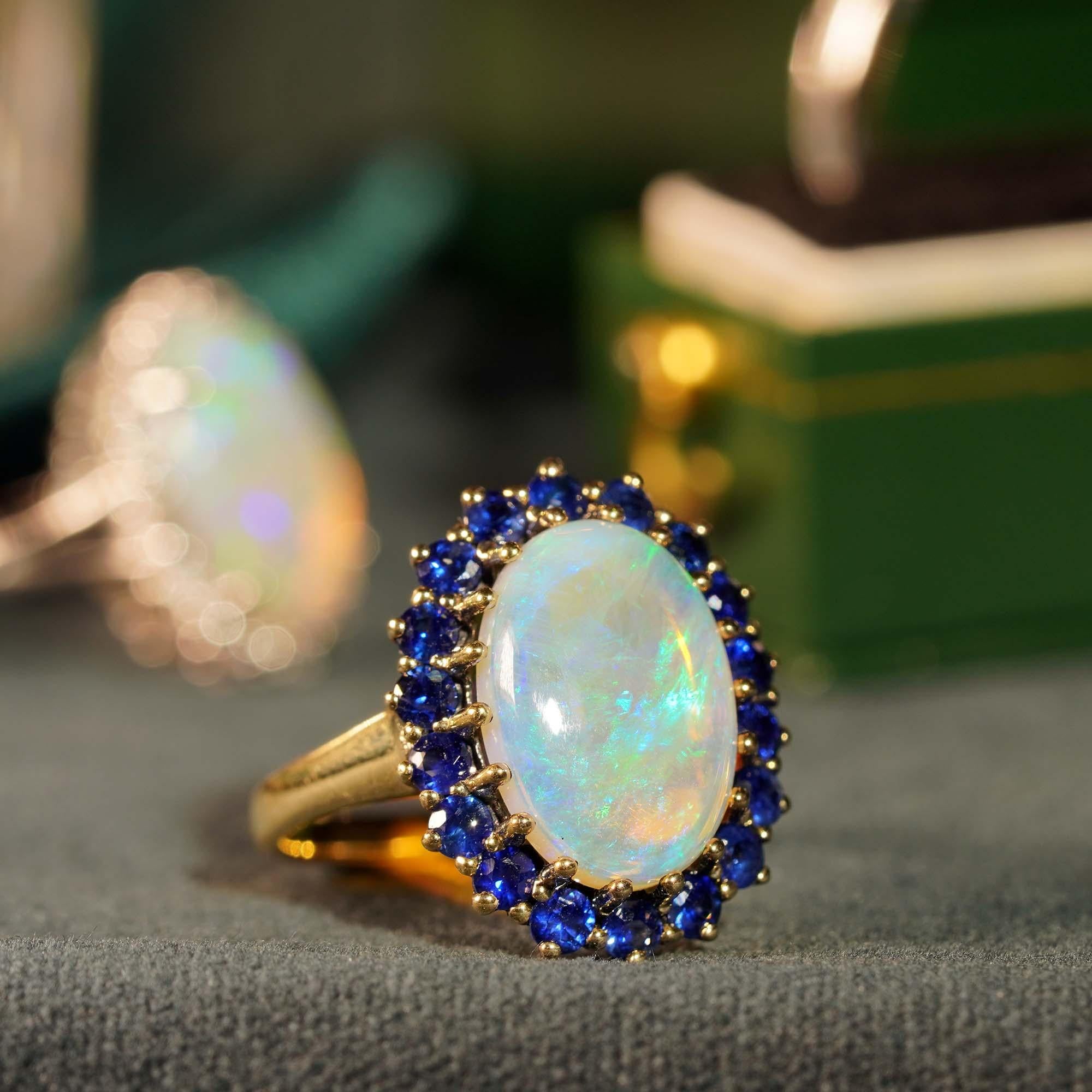 This beautiful ring is a classic vintage inspired style, the halo ring features play-of-color oval 3.43 carat opal for its center, surrounded by eight-teen blue sapphires. This would make a wonderful statement ring.

Ring Information
Style:
