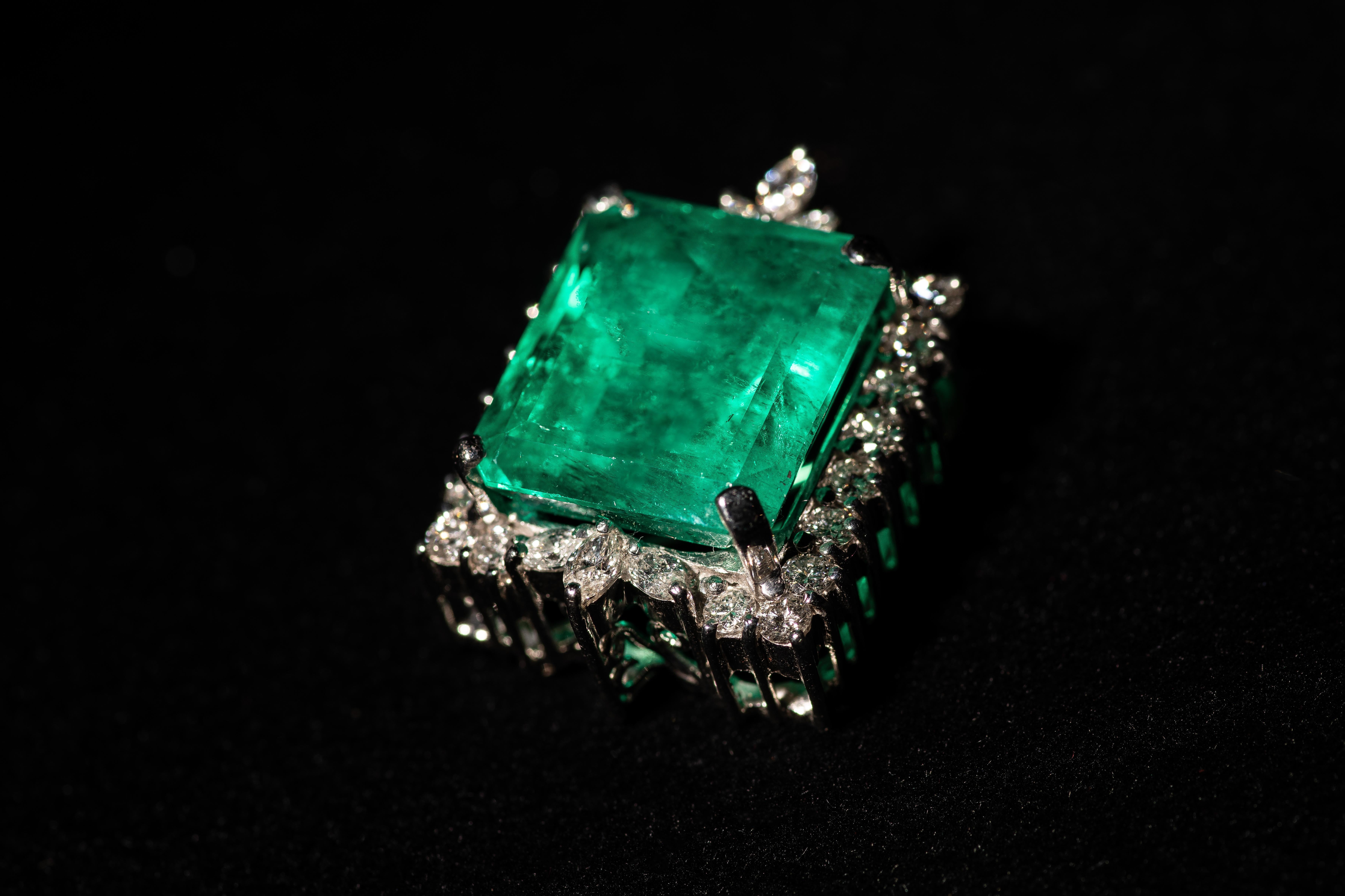 A stunning emerald brooch pin, featuring a magnificent 34.30 Colombian emerald cut emerald surrounded by diamonds, all set in 18k white gold.

The large emerald is AGL certified as natural, green in color, with minor clarity enhancement. A copy of