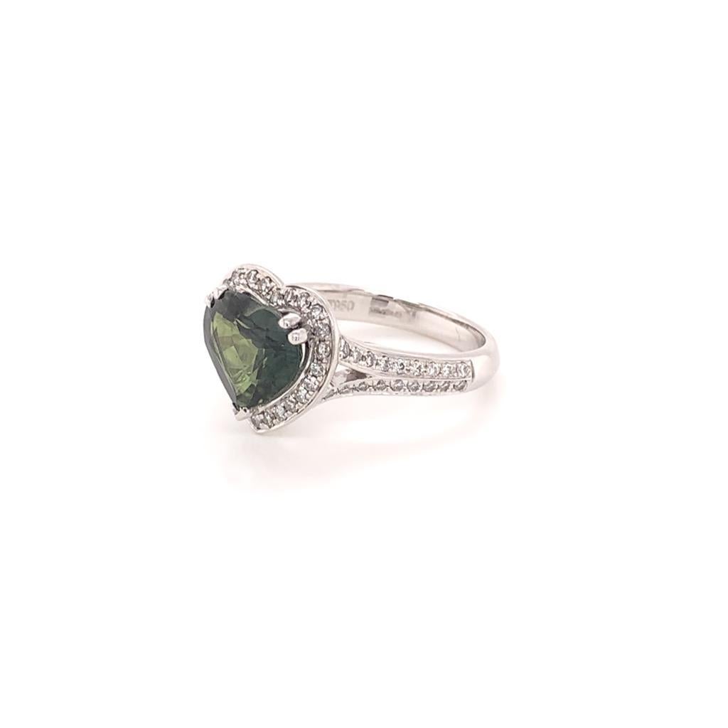 The Deep hues of this Striking Heart-Shaped 3.44 Carat Green Sapphire are Beautifully complimented by the Round Brilliant Diamonds that surround it, weighing 0.27 Carats and set in Platinum. The contrast between the colours add to the sophistication