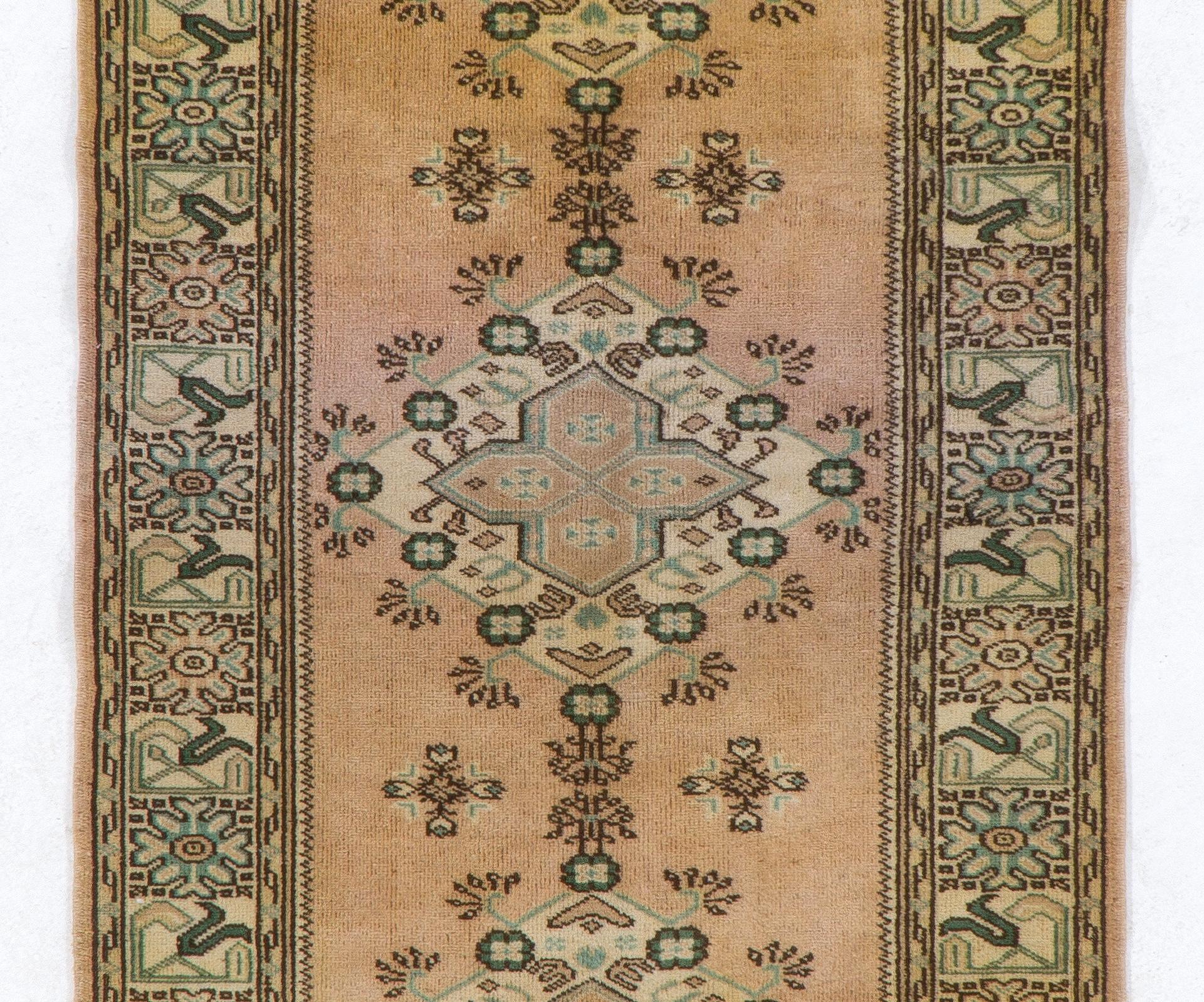 A vintage Turkish runner rug with a linked medallions design against a faded salmon background and a border in green, blue and ivory decorated with medallion like floral heads and tulip motifs.

The rug was hand-knotted in the 1960s with wool pile
