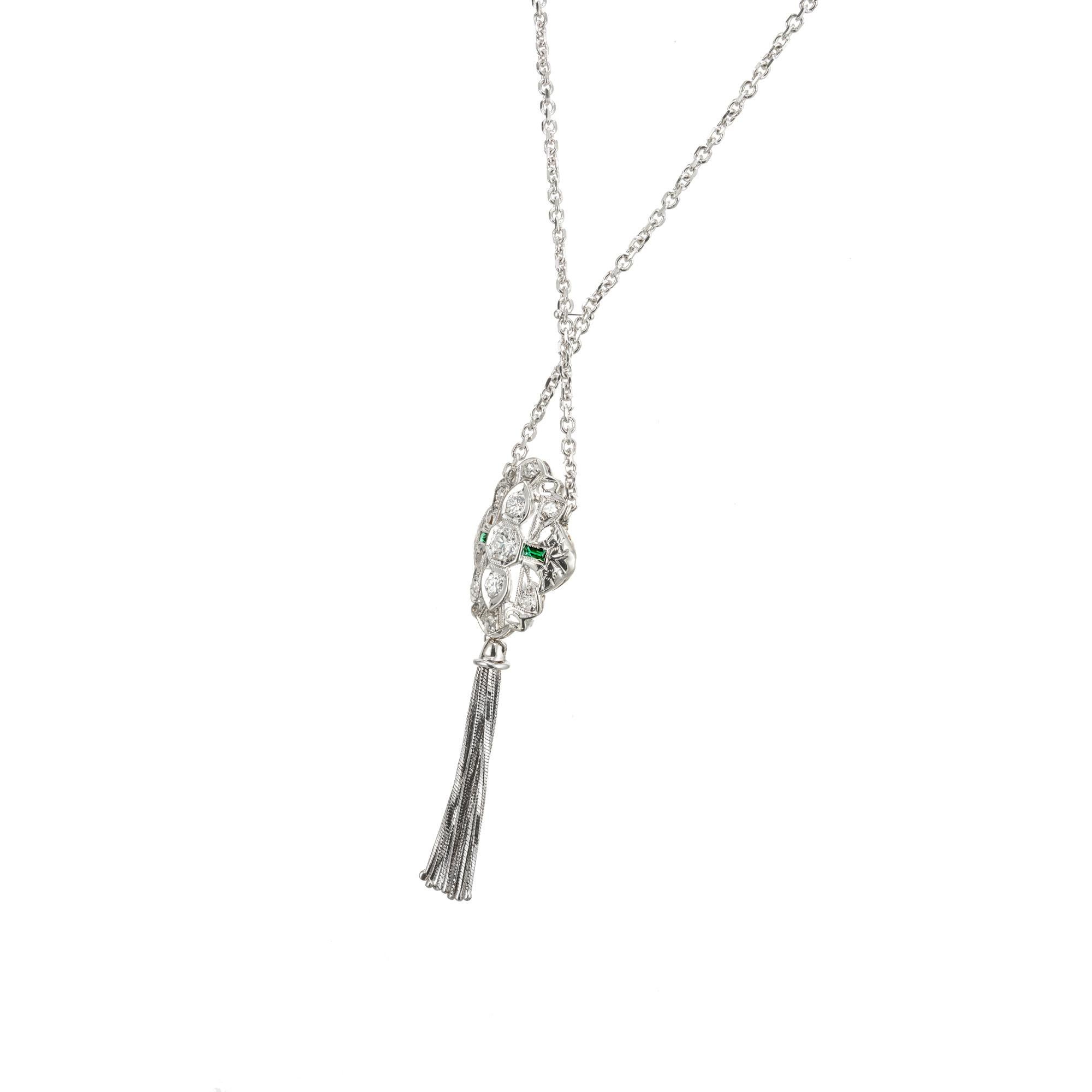 1930’s style Art Deco pendant necklace. The center piece of this necklace is the engraved, pierced and filigree 14k white gold pendant which is set with 9 round European cut diamonds and accented by  2 green synthetic French cut emeralds. 7 tassels