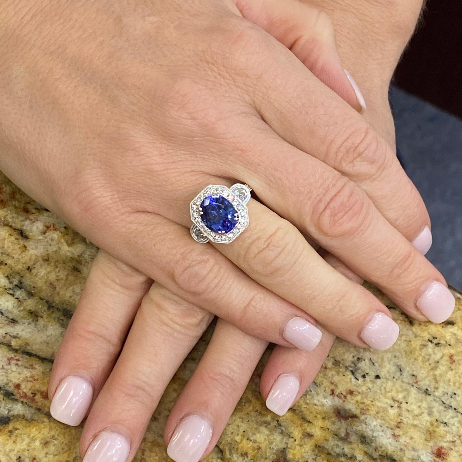 Beautiful oval tanzanite diamond ring fashioned in 18 karat yellow gold. The oval tanzanite weighs 3.50 carats and is set in a modern mounting featuring 2 half moon cut diamonds weighing approximately .50 carat total weight and another 22 round