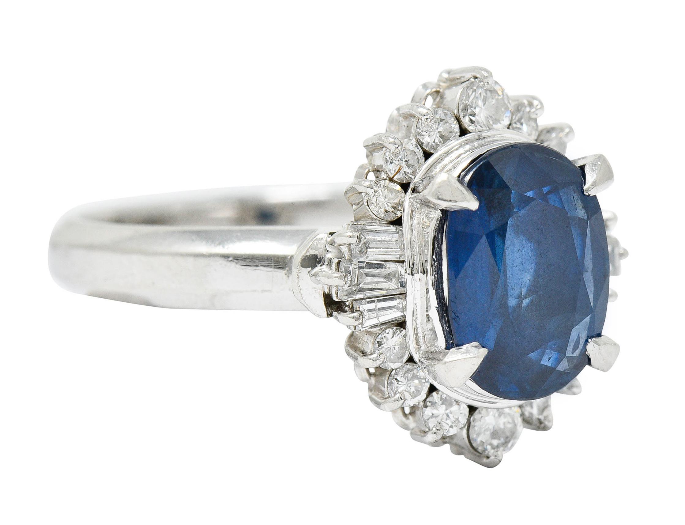 Cluster ring centers an oval cushion cut sapphire weighing approximately 2.94 carats

Talon set with transparent medium-dark royal blue color

Surrounded by diamond halo comprised of baguette and round brilliant cut diamonds

Weighing in total