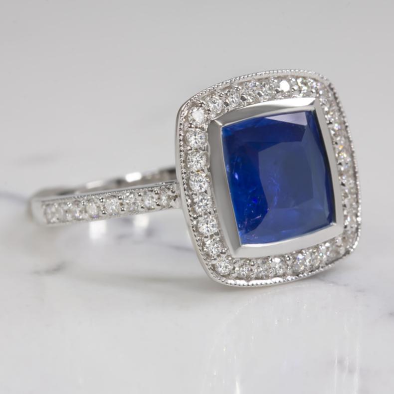 Ring with a royal blue sapphire in a luxurious diamond-encrusted 14k white gold setting! The 3.08ct cushion cut sapphire center has a stunning royal blue color. It is a beautiful true blue measuring approximately 9mm square, the sapphire looks