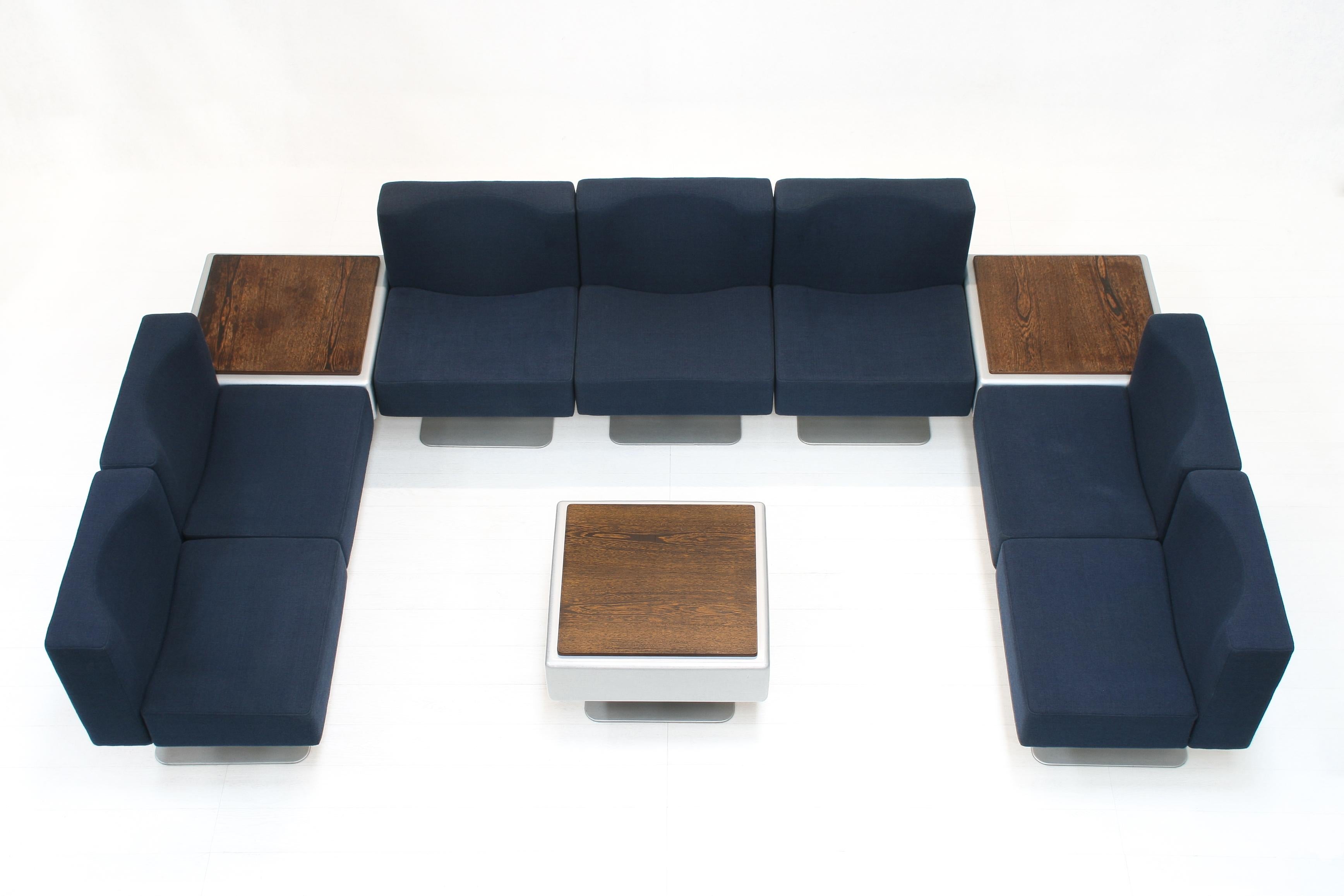 This large set consists of 7 dark blue upholstered chairs with aluminium base and 3 fiberglass table with veneer top and aluminium base. 

The square shape allows endless creative combinations for a lounge or waiting area.

Each element measures