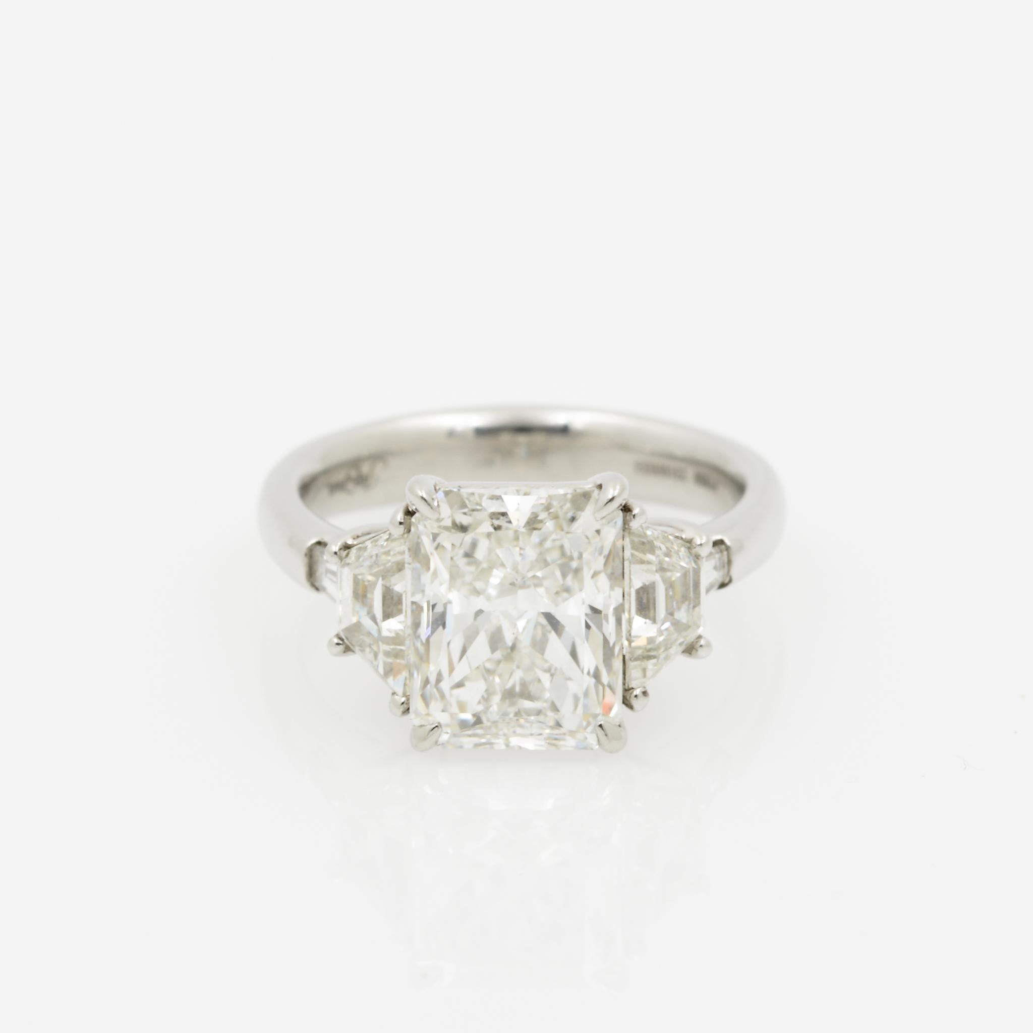 This platinum five-stone ring features a 3.51 carat GIA certified radiant cut diamond with G coloring and SI1 clarity at its center. On either side of the main stone are two trapezoid diamonds with a combined total weight of 0.90 carats, as well as