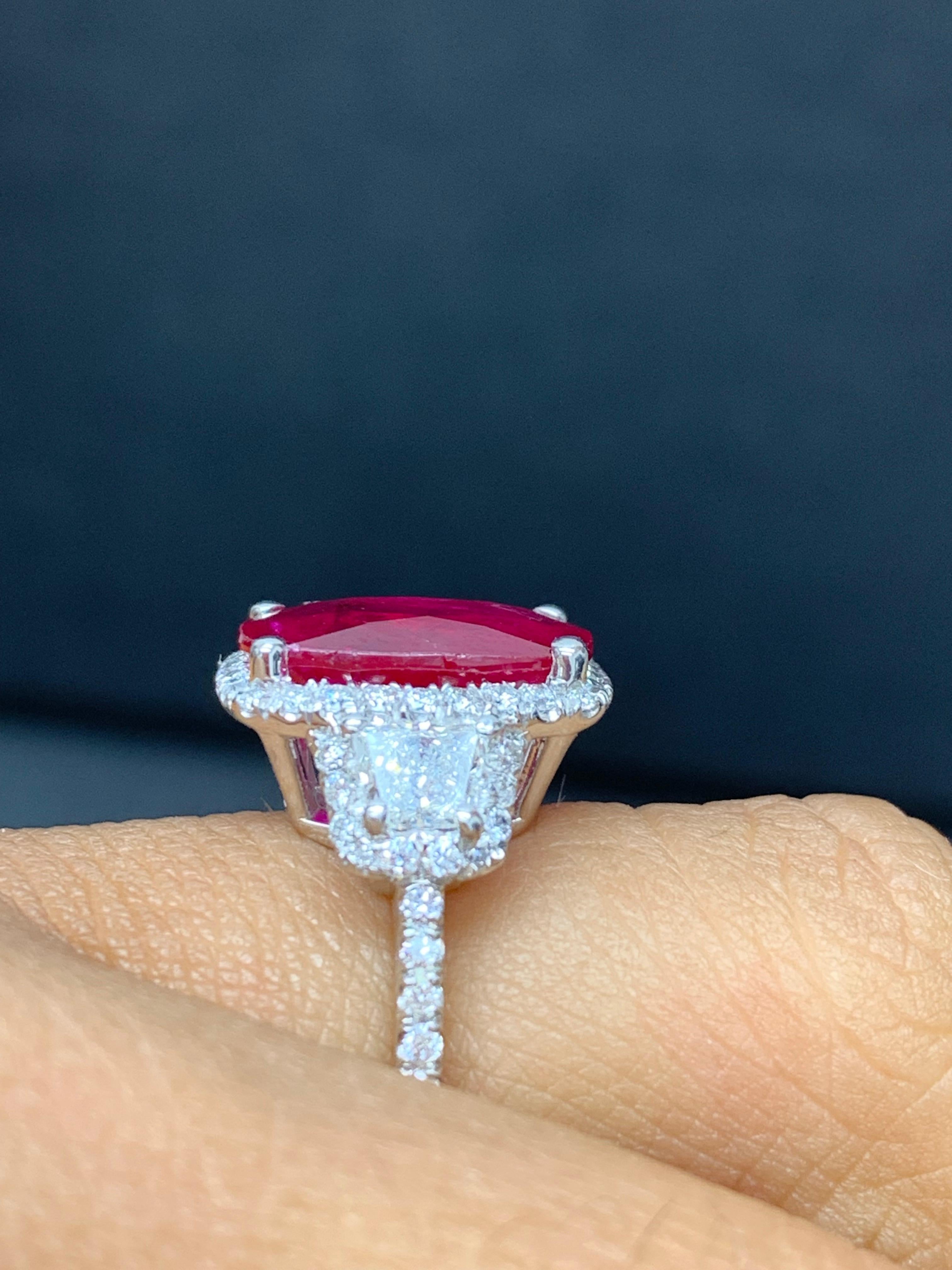 This three-stone ring is set with a 3.52-carat cushion cut ruby center stone flanked with 2 brilliant-cut trapezoid diamond side stones weighing 0.31 carats.  A single row of round brilliant diamonds accent the center and side stones. The total