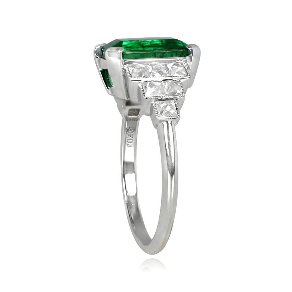 This platinum ring boasts a dazzling 3.52-carat emerald-cut emerald, held in place by sturdy prongs. The center stone is accompanied by a graduated French-cut diamond design on each side, elegantly displayed in rectangular bezels along the