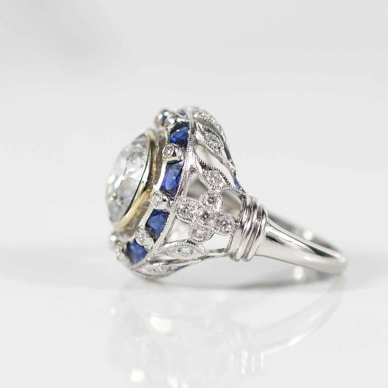 Step into the glamour of the Art Deco era with this captivating engagement ring, featuring a stunning 3.52 carat old European cut diamond as its centerpiece. Encircled by a halo of vibrant sapphires totaling approximately 1.19 carats and accentuated
