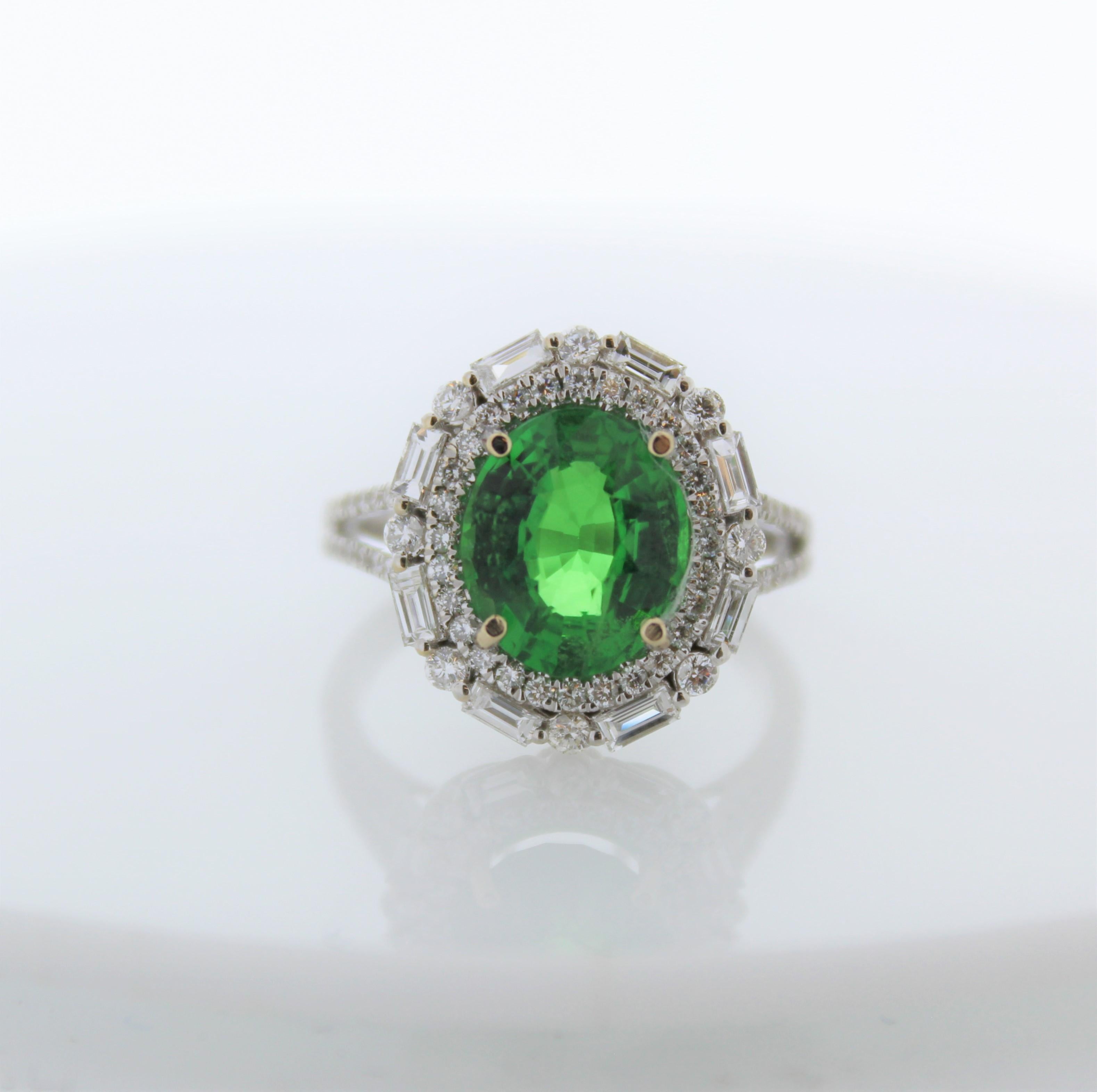 This ring holds a vibrant green tsavorite garnet from Tanzania. The weight of this tsavorite is 3.54 carats. Its luster and transparency are excellent. 84 sparkling mixed cut diamonds surround this tsavorite in a glittering halo cluster and down the
