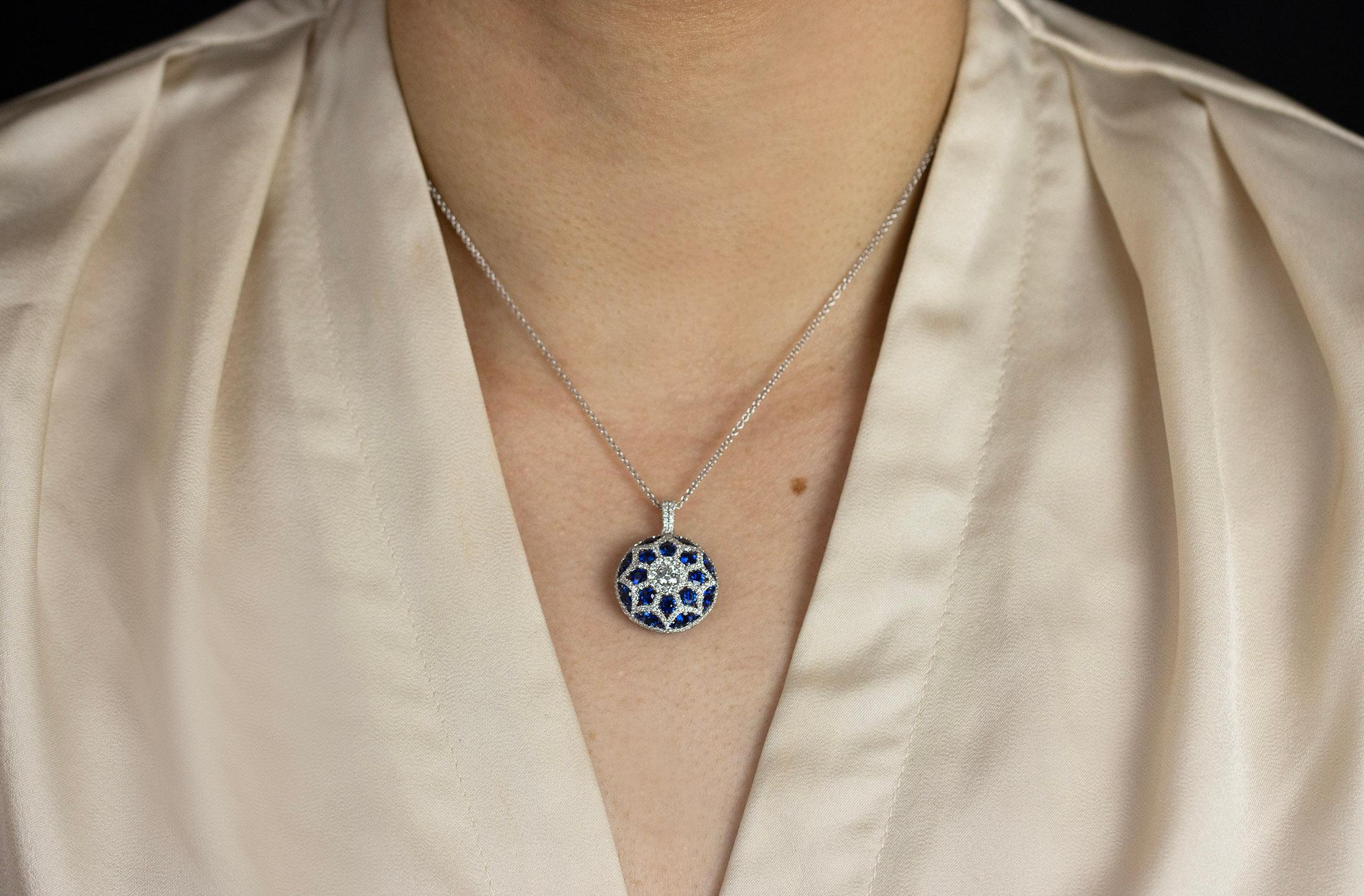 A fashionable circle pendant necklace with a convex design, showcasing a brilliant round diamond center stone, Surrounded by blue sapphires and diamonds in a unique and chic design. Diamonds weigh 0.97 carats total, sapphires weigh 2.58 carats