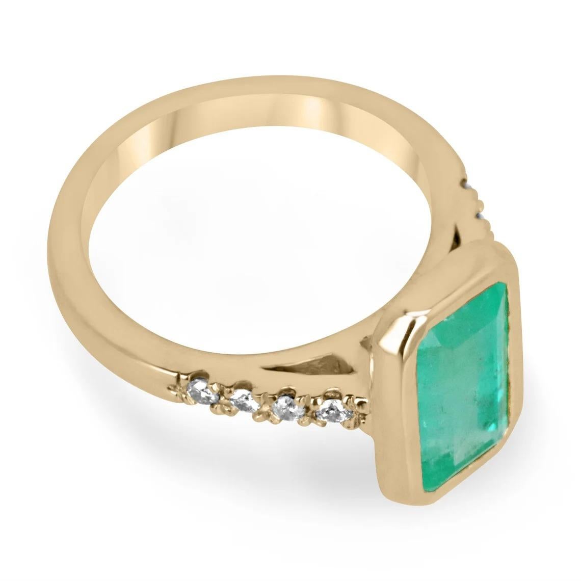 A glowing Colombian emerald bezel and diamond accent ring. This spectacular piece features an elongated emerald cut emerald from the best mines in the world, Colombia. The gemstone showcases a sweet bluish-green color that is vivacious and lustrous.