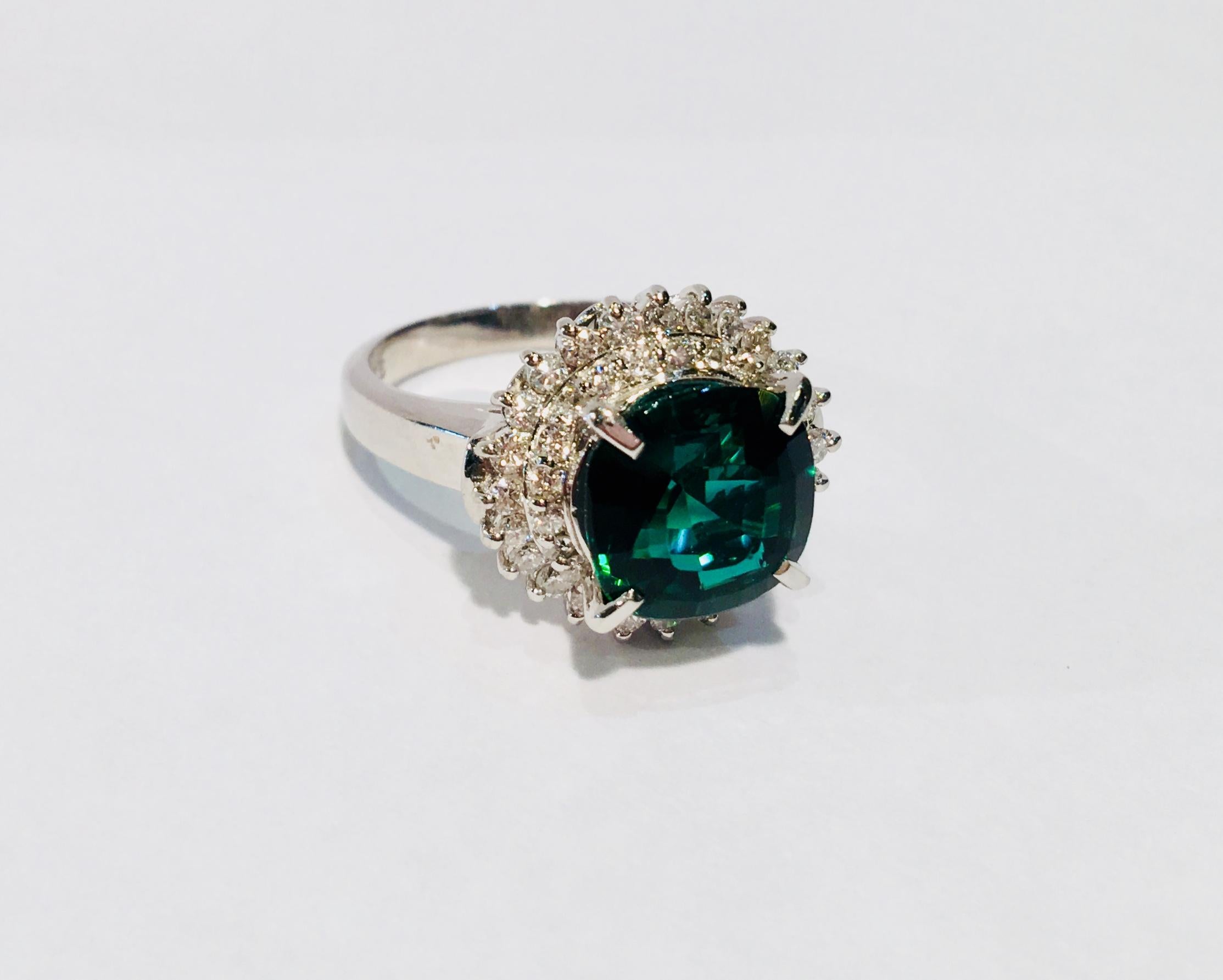 Deeply saturated, blue green indicolite tourmaline is cushion cut, prong set and surrounded by a sparkling double halo of .66 carats round brilliant white diamonds.  Diamonds are SI in clarity with a color of H-I.

Face of indicolite measures 9.50
